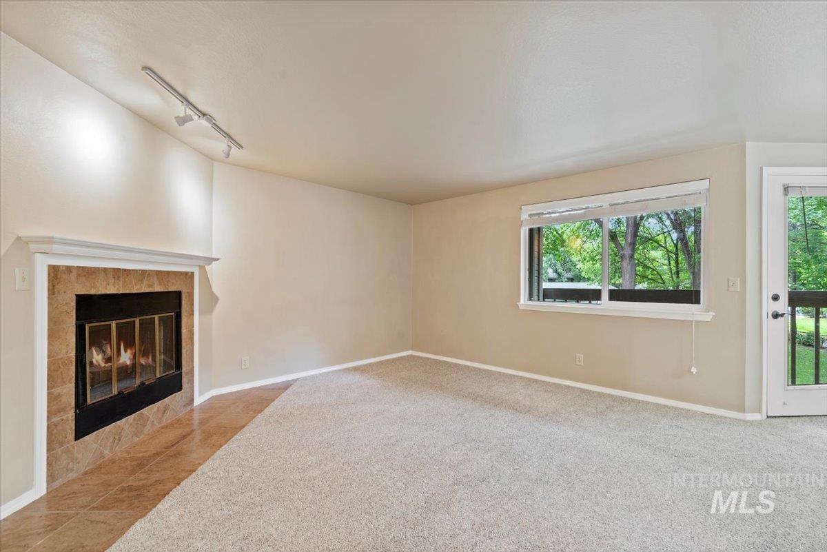 Unfurnished living room featuring rail lighting, a tile fireplace, and light carpet
