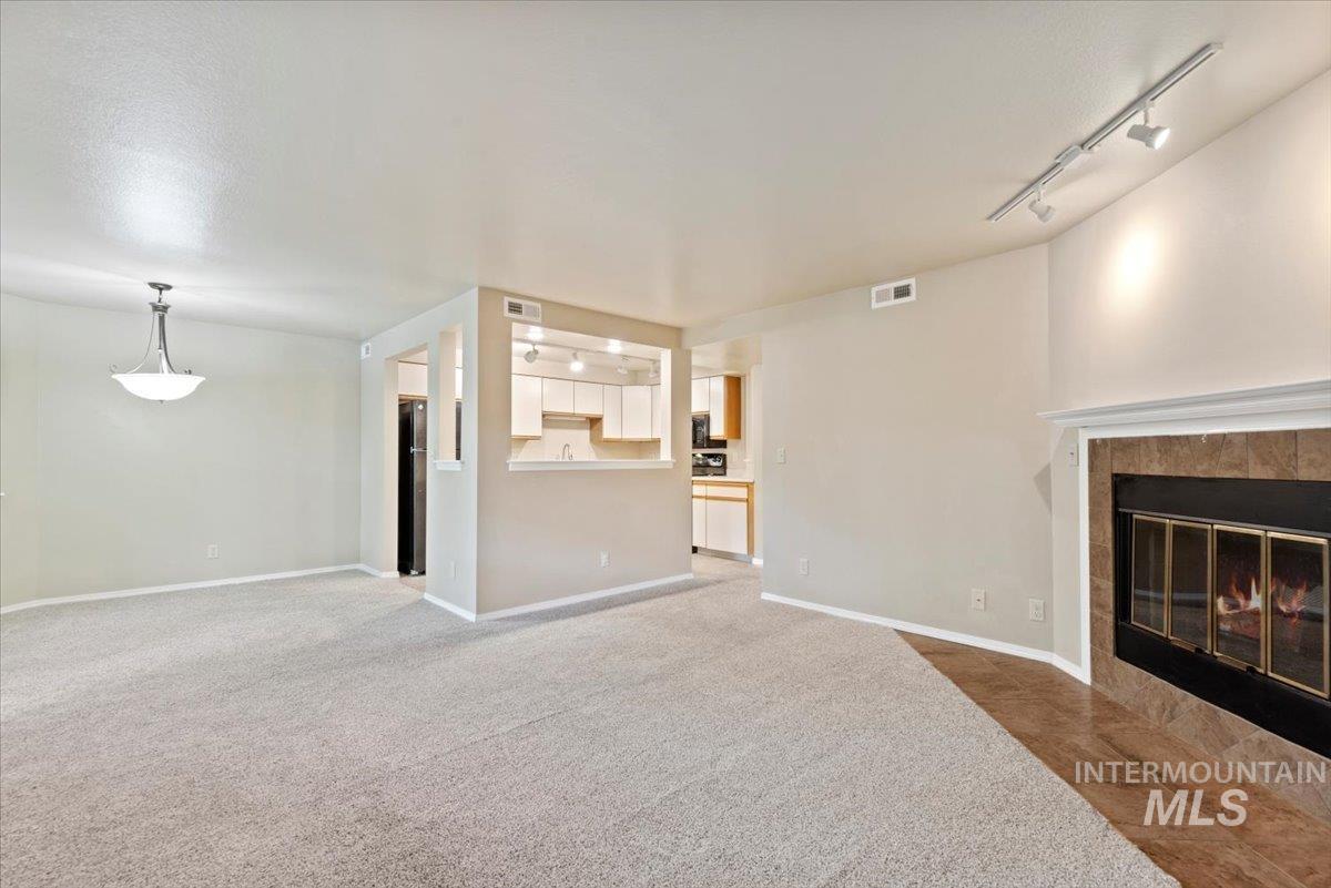 Unfurnished living room featuring track lighting, a tiled fireplace, and carpet floors