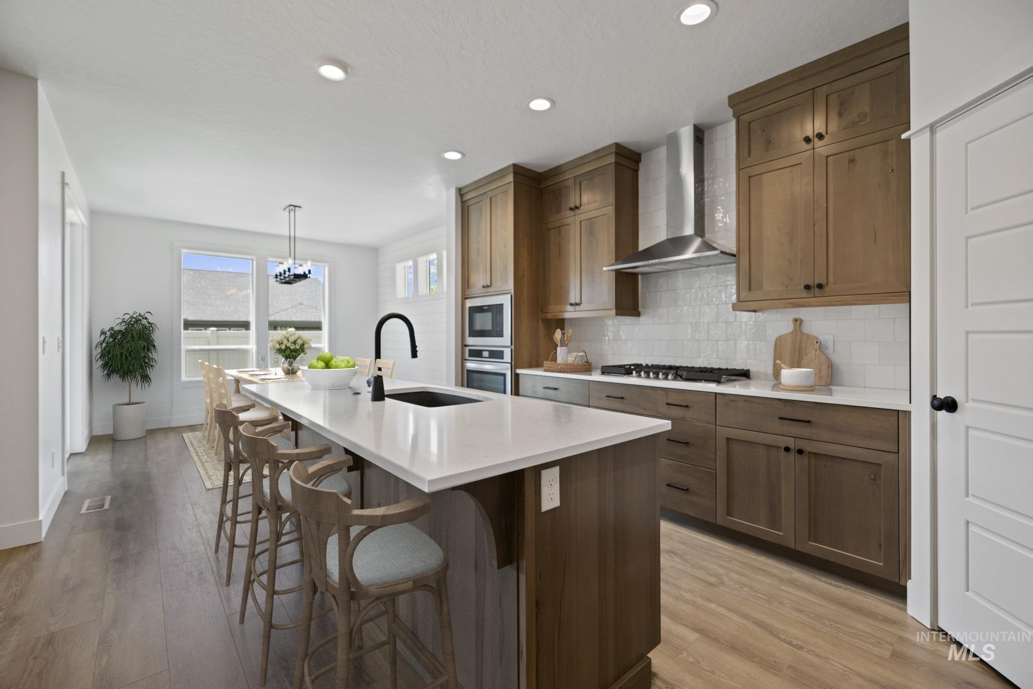 Kitchen with wall chimney exhaust hood, a kitchen island with sink, backsplash, a kitchen breakfast bar, and light countertops