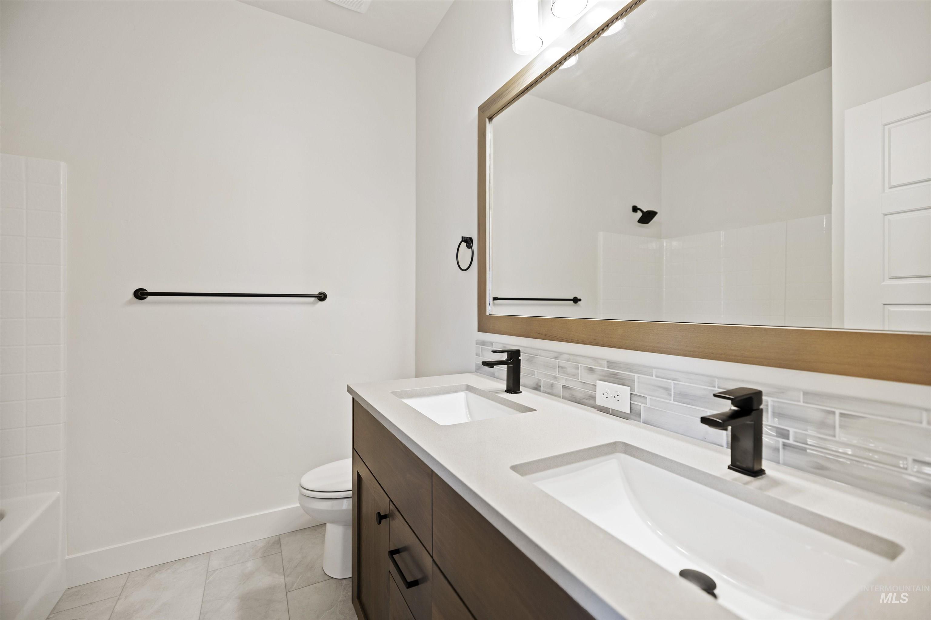 Bathroom featuring double vanity, decorative backsplash, and tub / shower combination
