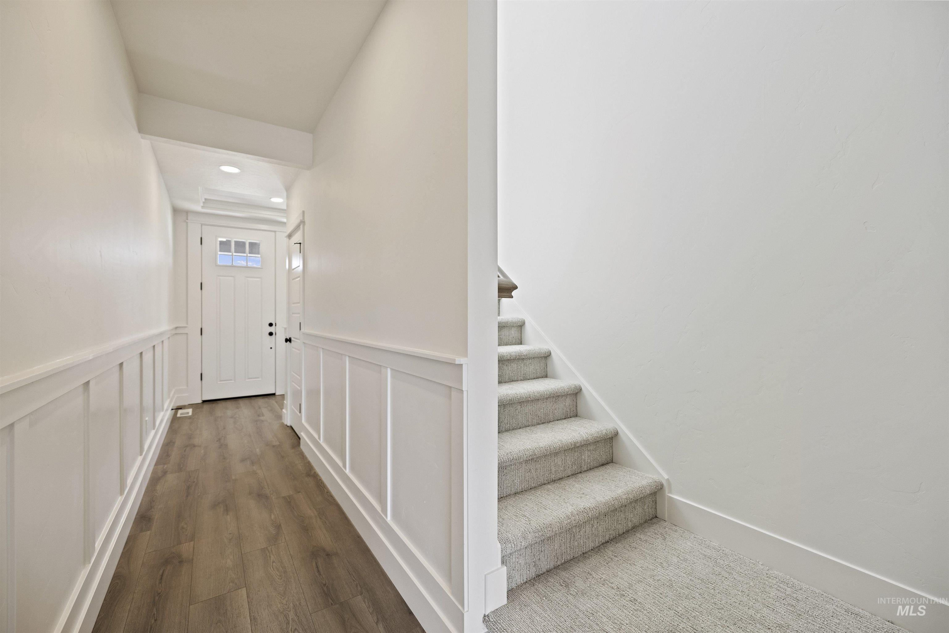 Hallway featuring wood finished floors, stairs, a wainscoted wall, a decorative wall, and recessed lighting