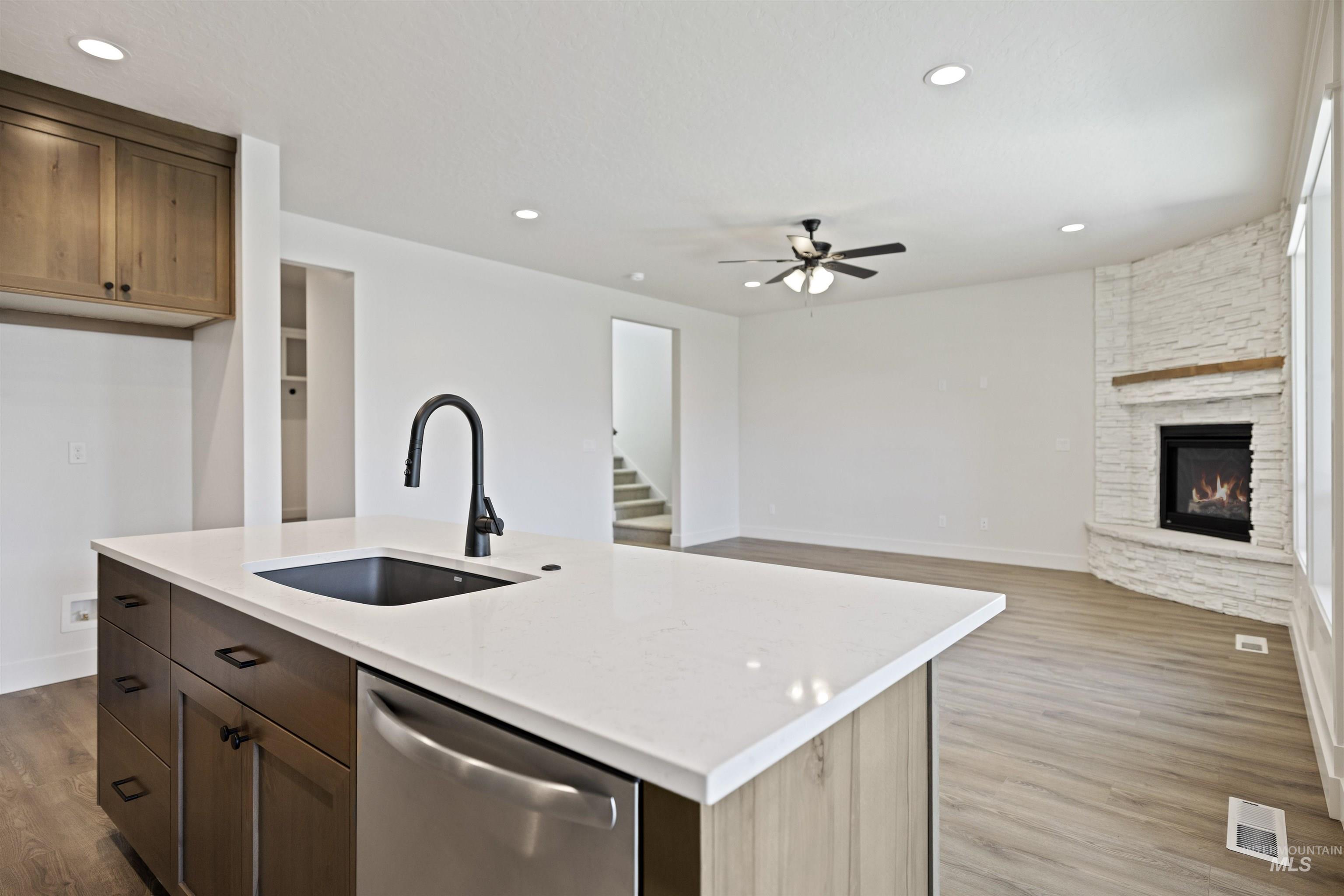 Kitchen featuring stainless steel dishwasher, open floor plan, a ceiling fan, a stone fireplace, and wood finished floors