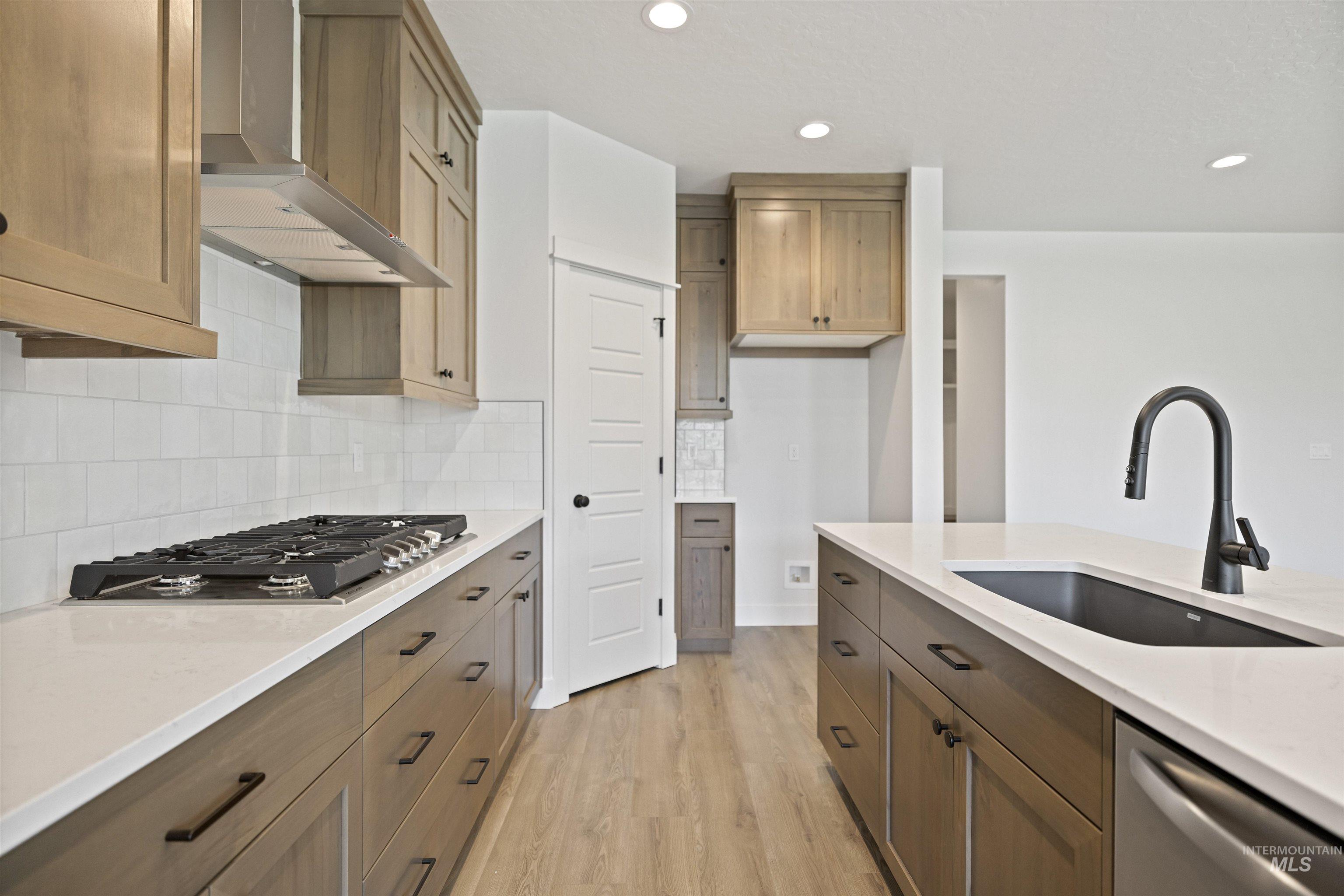 Kitchen featuring wall chimney range hood, appliances with stainless steel finishes, light wood finished floors, light countertops, and decorative backsplash