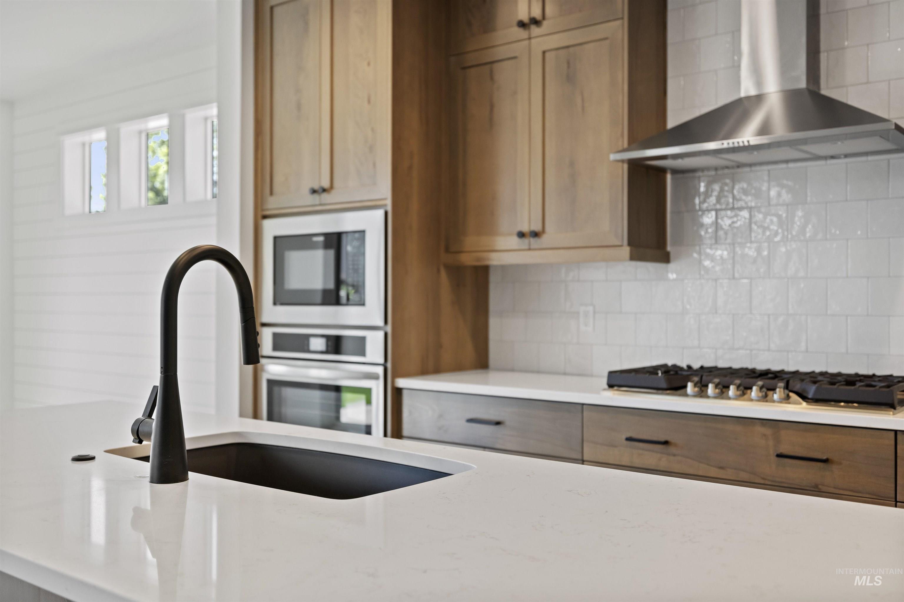 Kitchen featuring wall chimney range hood, stainless steel appliances, backsplash, and light stone countertops