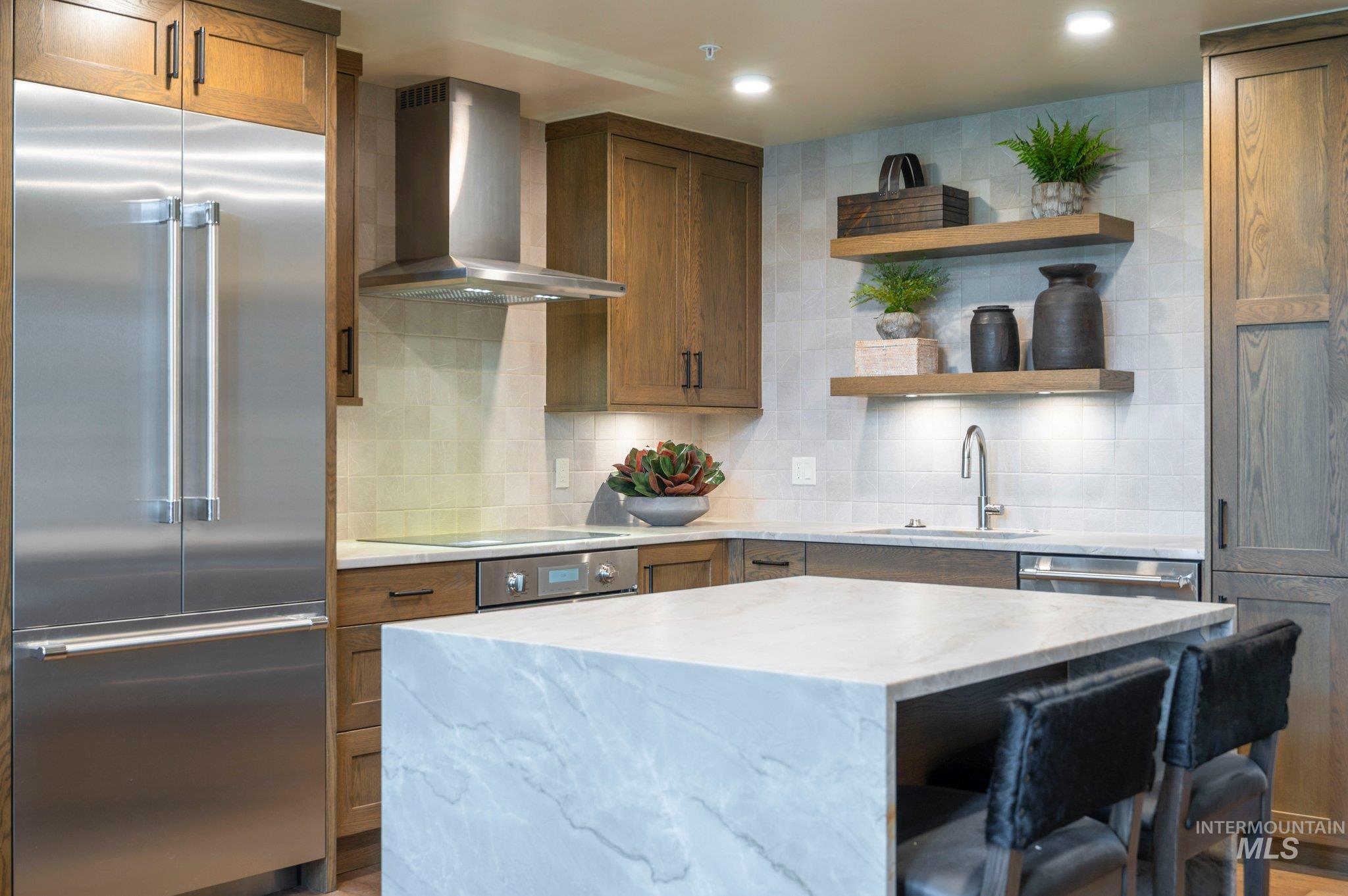 Kitchen with appliances with stainless steel finishes, tasteful backsplash, wall chimney range hood, open shelves, and light stone countertops
