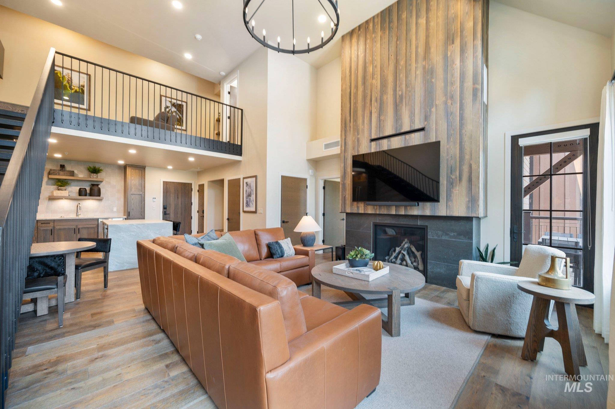 Living room with light wood-type flooring, recessed lighting, a glass covered fireplace, and a high ceiling