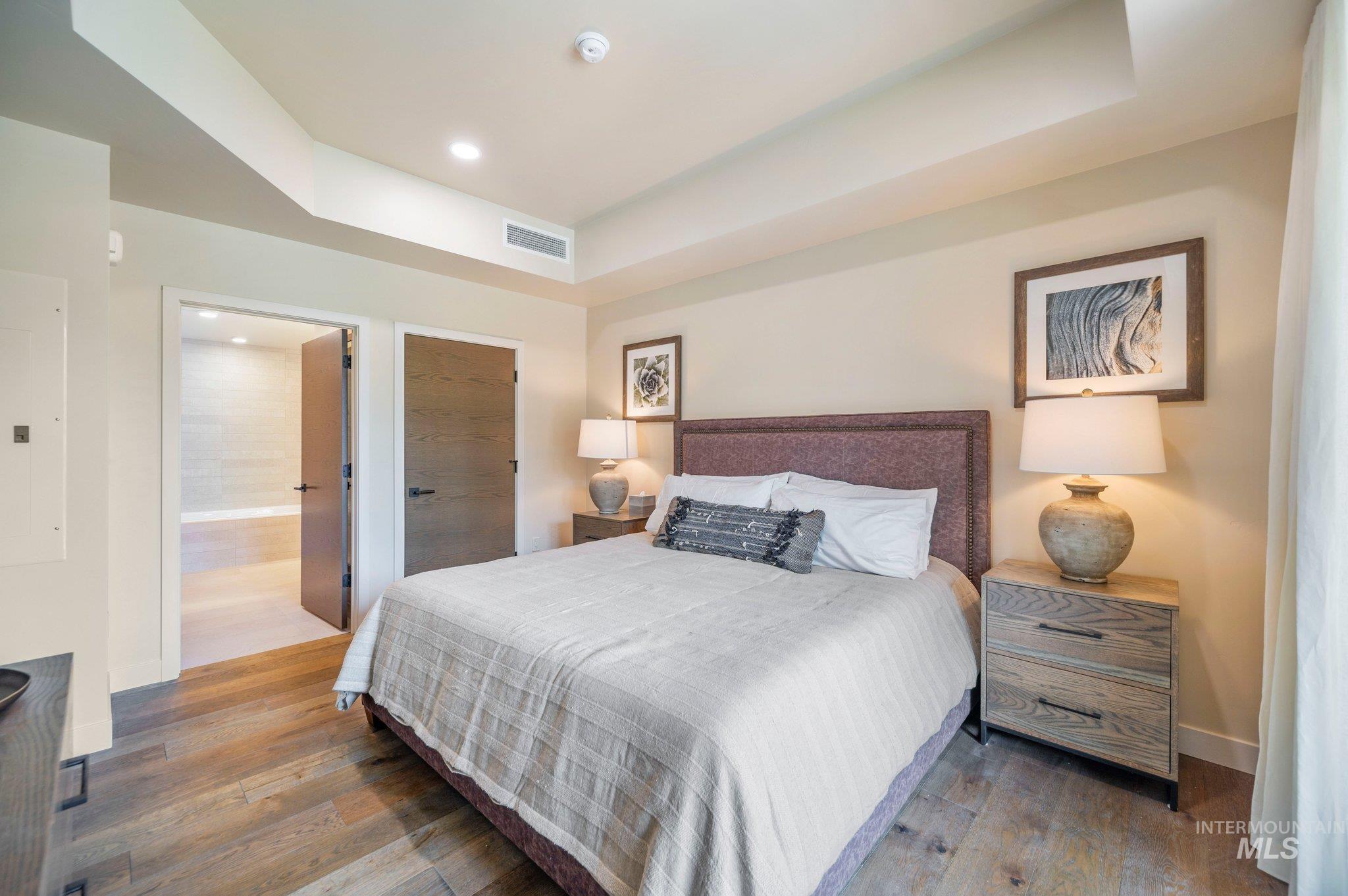 Bedroom with a raised ceiling, wood-type flooring, electric panel, recessed lighting, and a closet