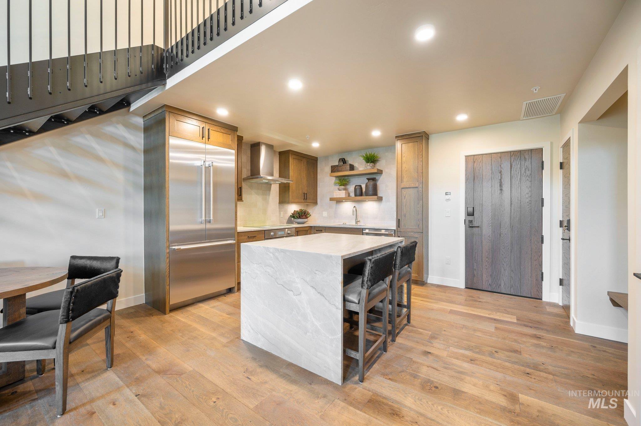 Kitchen with open shelves, built in refrigerator, light stone countertops, recessed lighting, and a kitchen breakfast bar