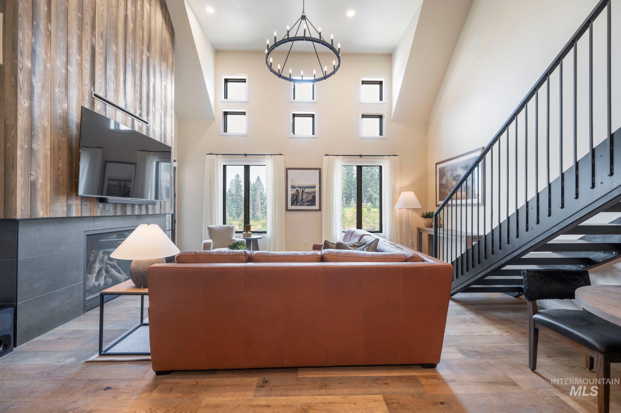 Living room featuring light wood-style floors, a towering ceiling, a chandelier, a fireplace, and stairs