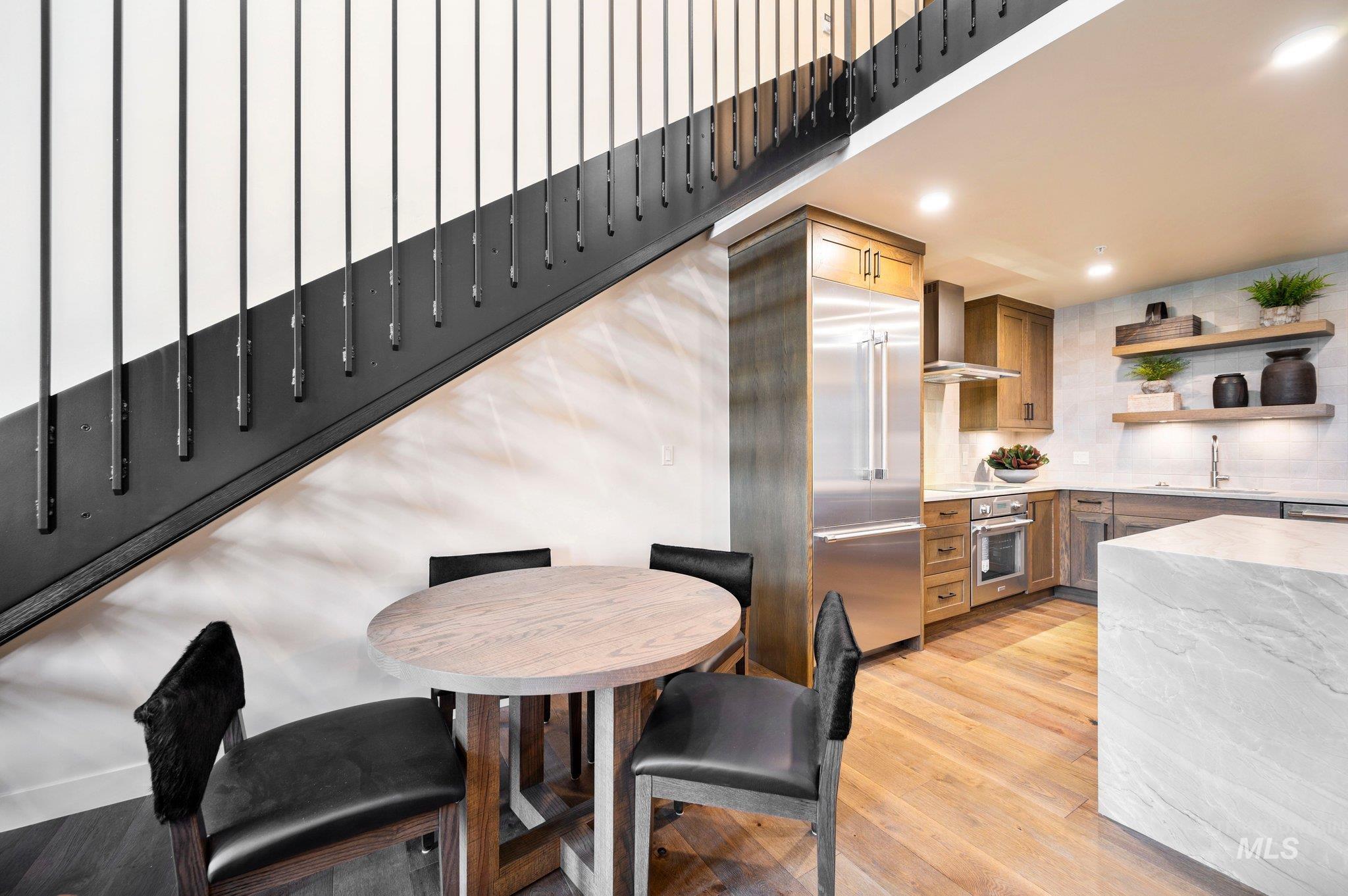 Kitchen featuring light stone countertops, open shelves, light wood finished floors, stainless steel appliances, and wall chimney range hood