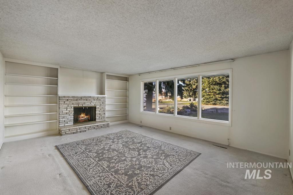 Unfurnished living room featuring a brick fireplace, carpet, a textured ceiling, and built in shelves