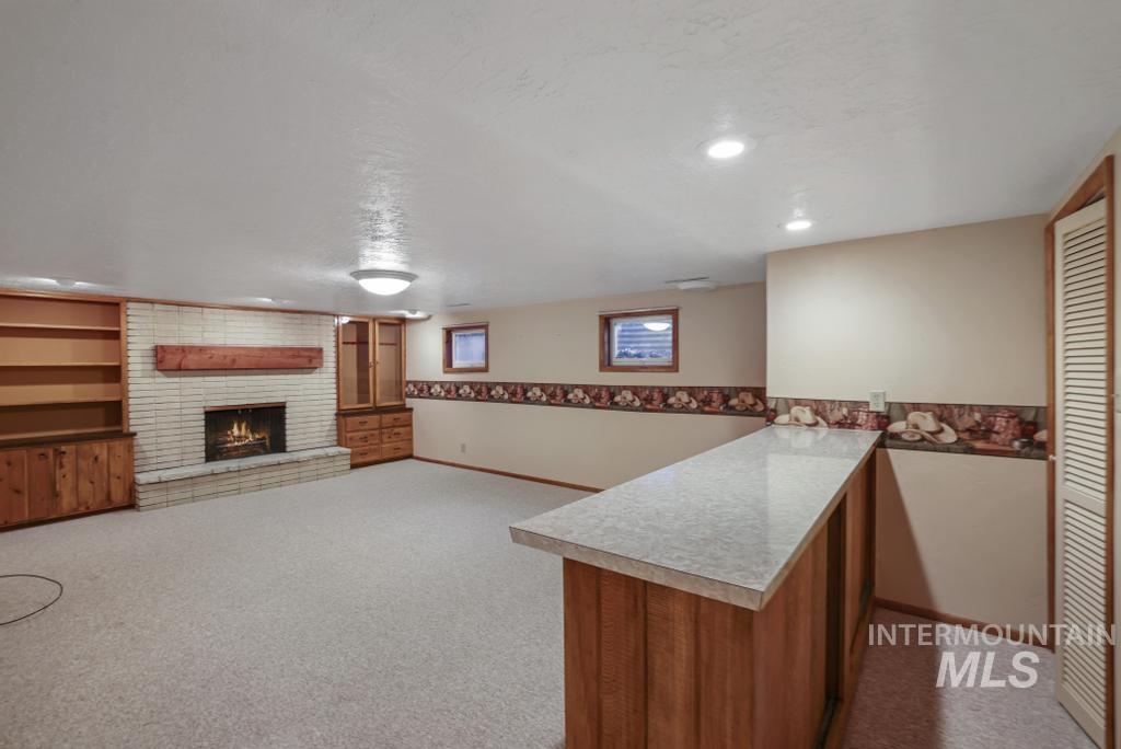 Bar area featuring a brick fireplace, light carpet, light countertops, a textured ceiling, and brown cabinets