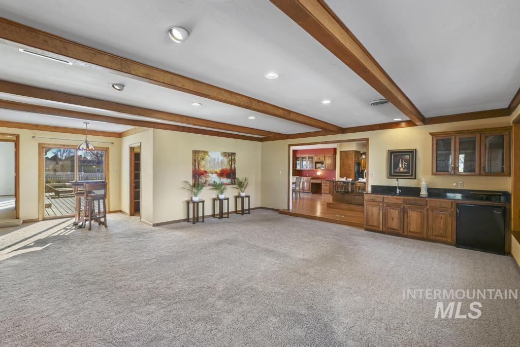 Living area featuring beamed ceiling, light colored carpet, recessed lighting, and wet bar