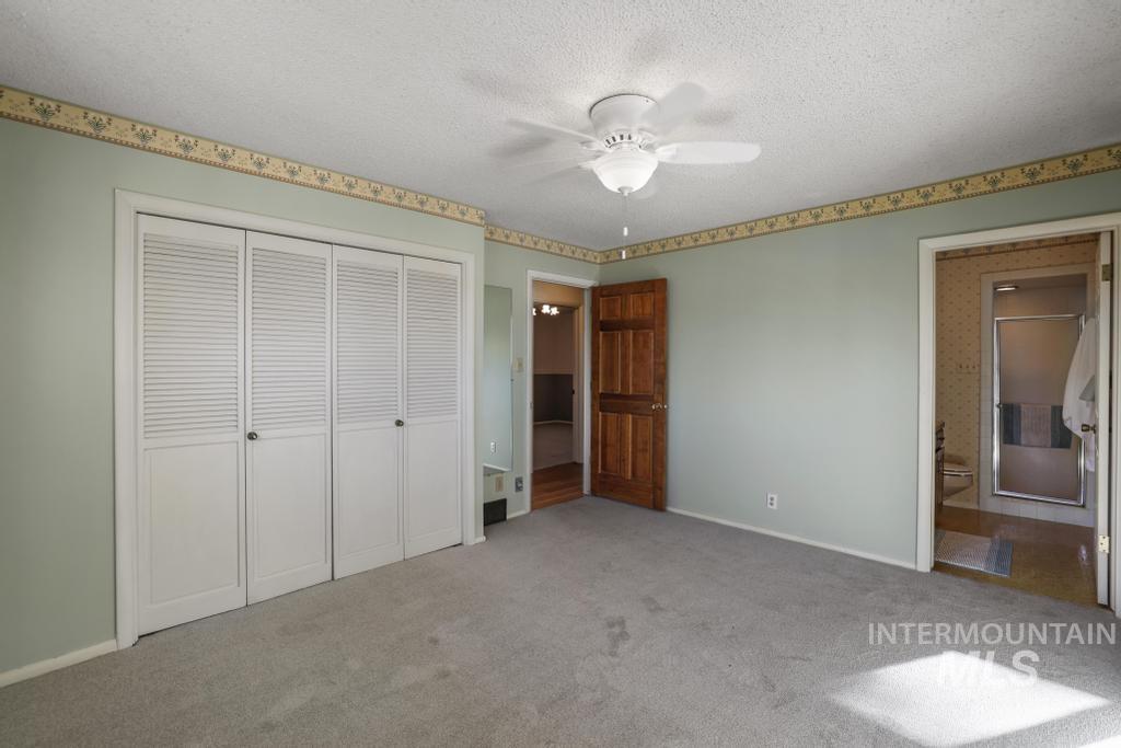 Unfurnished bedroom featuring carpet floors, a textured ceiling, a closet, ensuite bath, and a ceiling fan