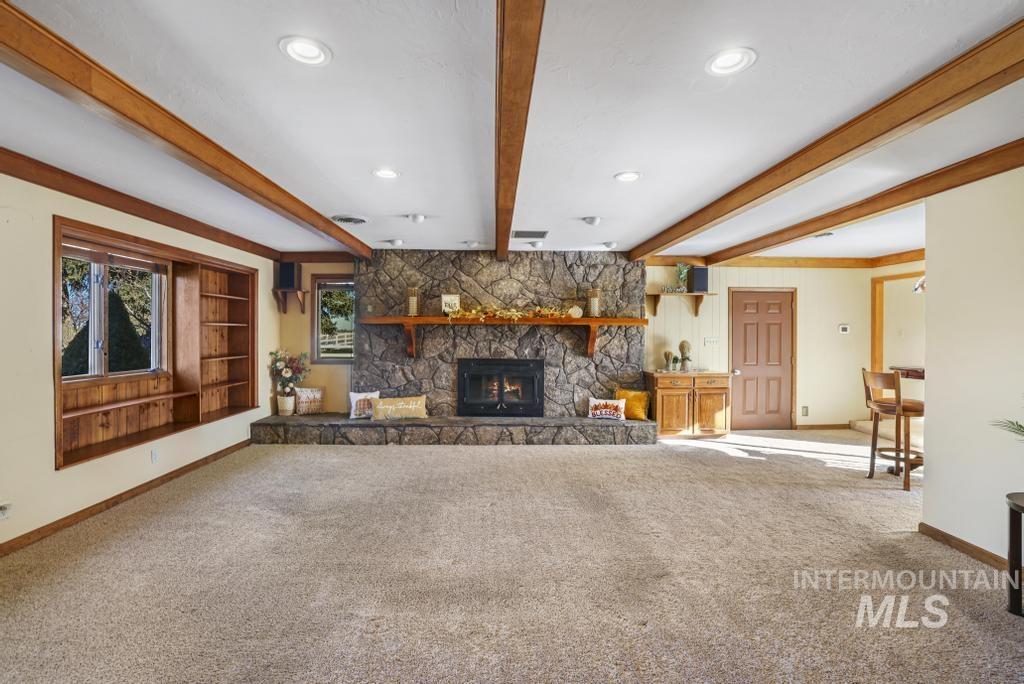 Unfurnished living room featuring carpet, beamed ceiling, a stone fireplace, and recessed lighting