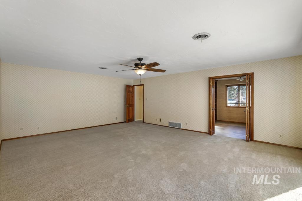 Empty room with wallpapered walls, light colored carpet, and ceiling fan