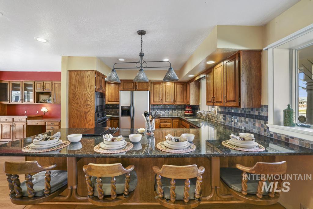 Kitchen with brown cabinets, backsplash, black appliances, a breakfast bar area, and dark stone countertops