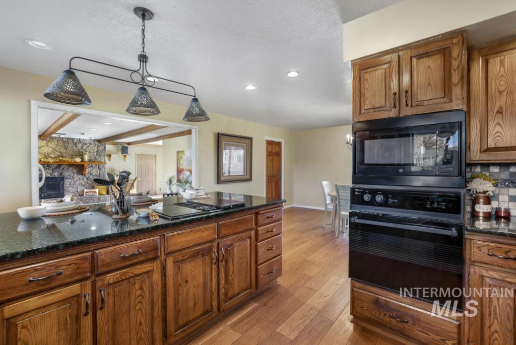 Kitchen featuring dark stone counters, brown cabinets, black appliances, light wood-style floors, and pendant lighting