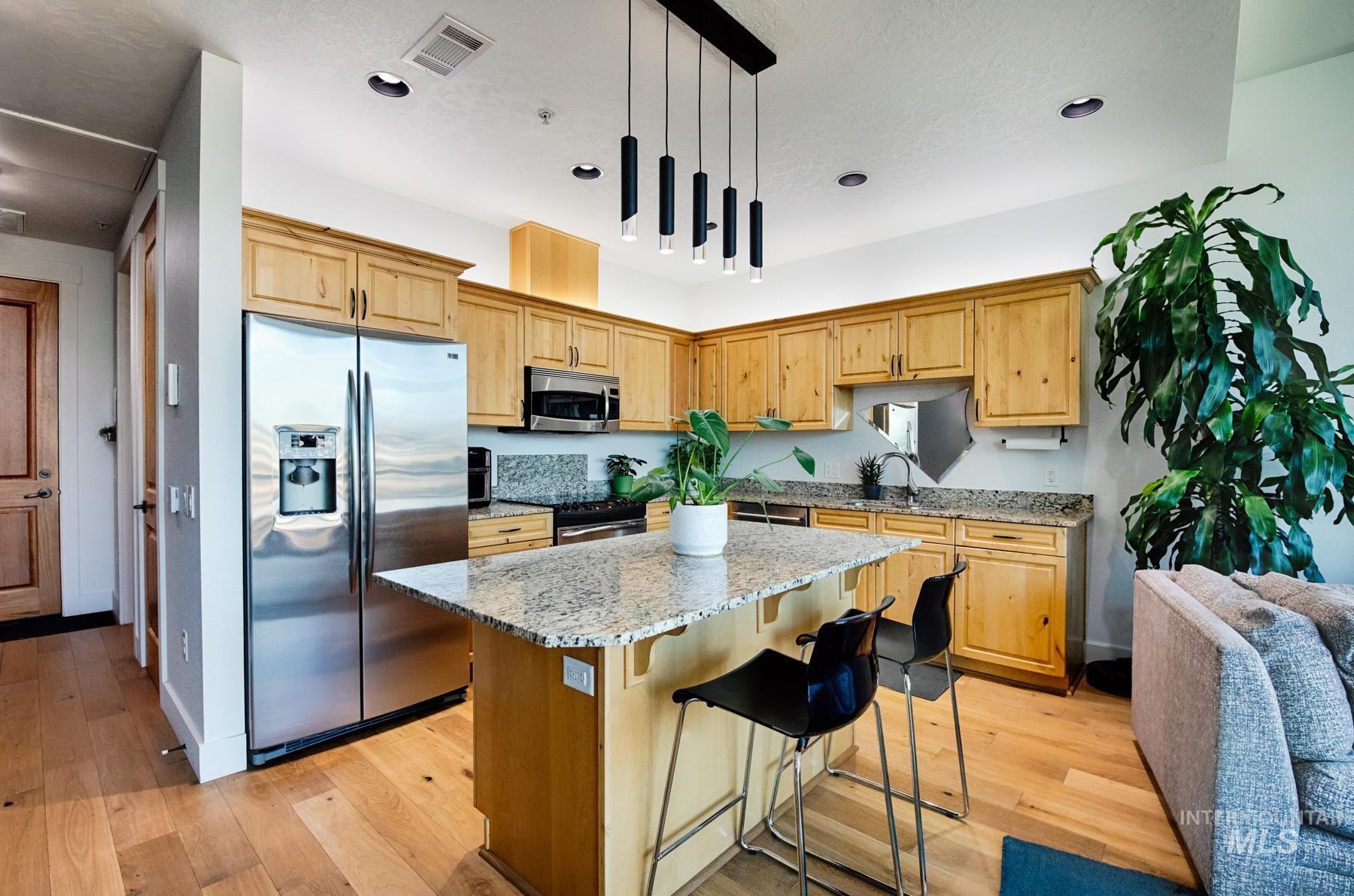 Kitchen with light stone countertops, stainless steel appliances, a breakfast bar, a kitchen island, and light wood-style floors