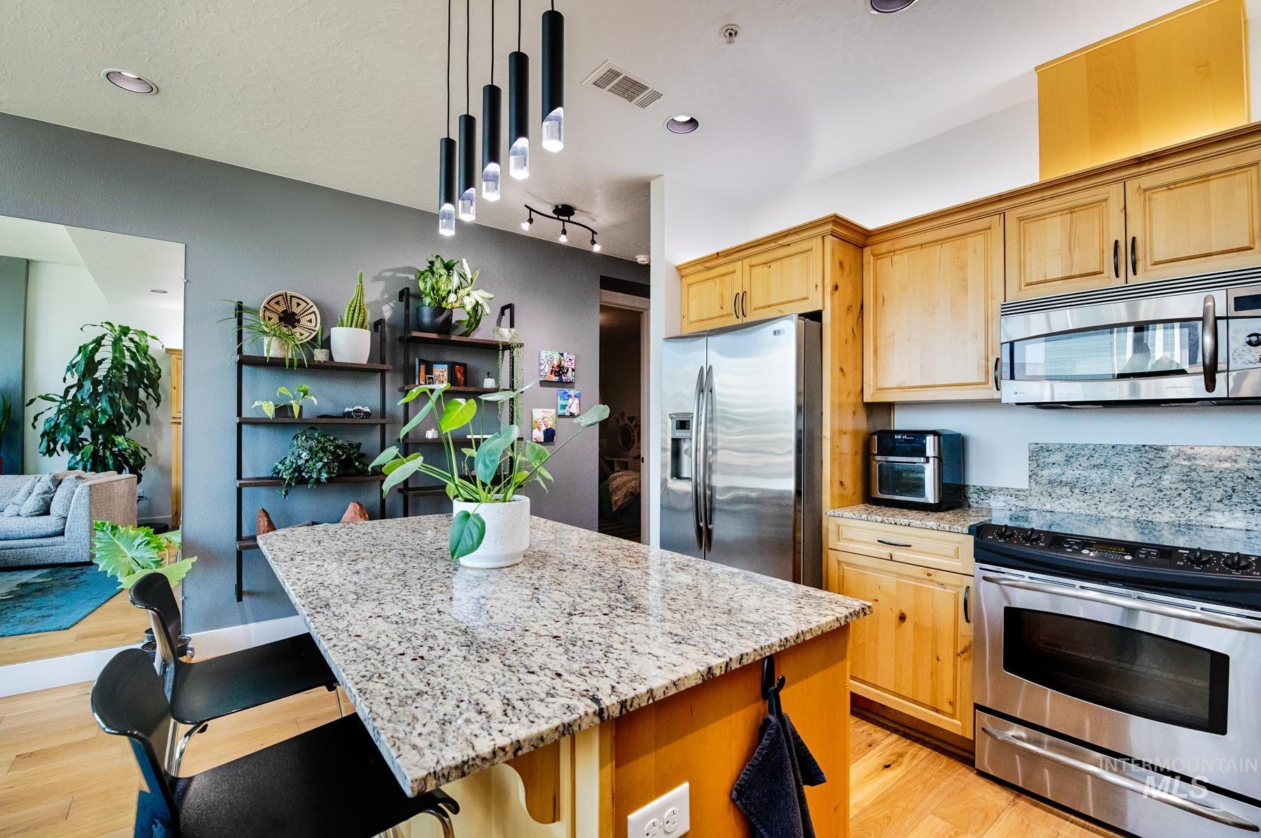 Kitchen featuring stainless steel appliances, light stone counters, a kitchen breakfast bar, pendant lighting, and a center island
