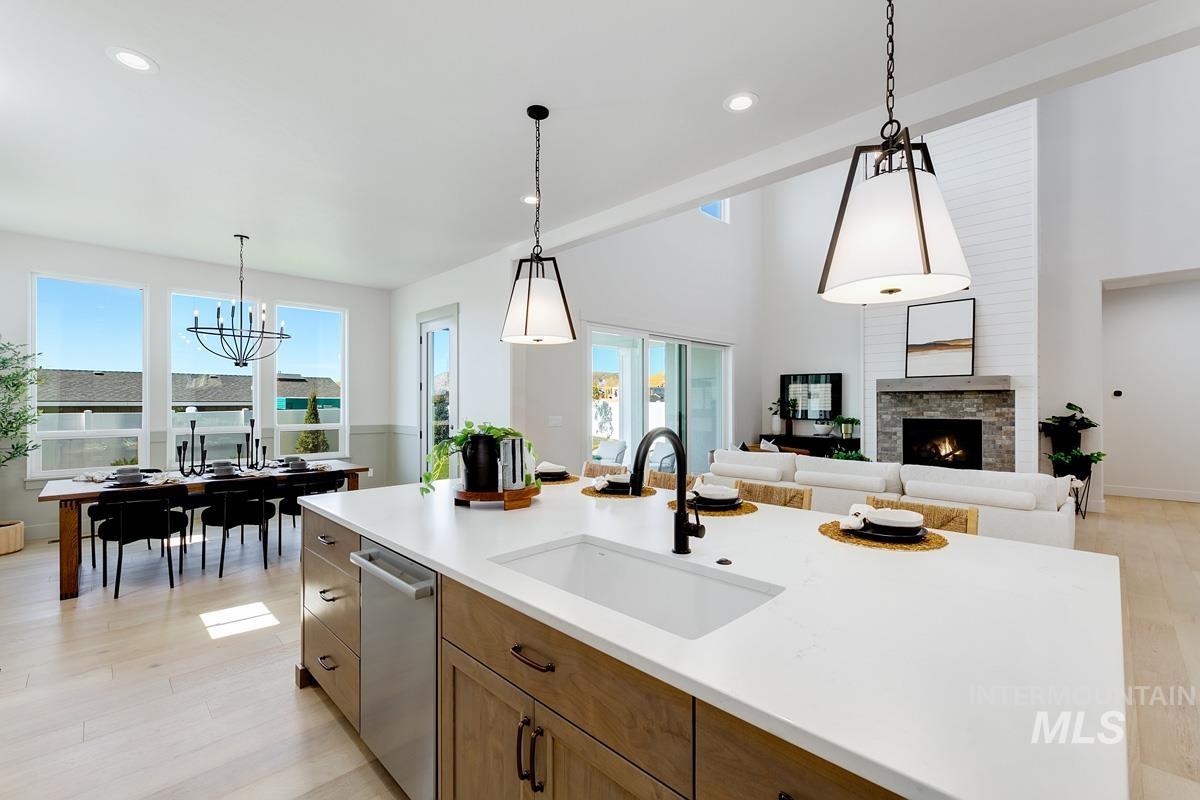 Kitchen with light wood finished floors, wood finish cabinets, a stone fireplace, stainless steel dishwasher, and open floor plan