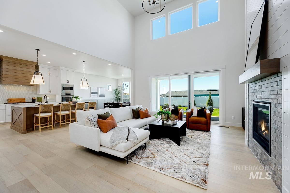 Living area featuring light wood-style flooring, a fireplace, hanging lights, and a high ceiling