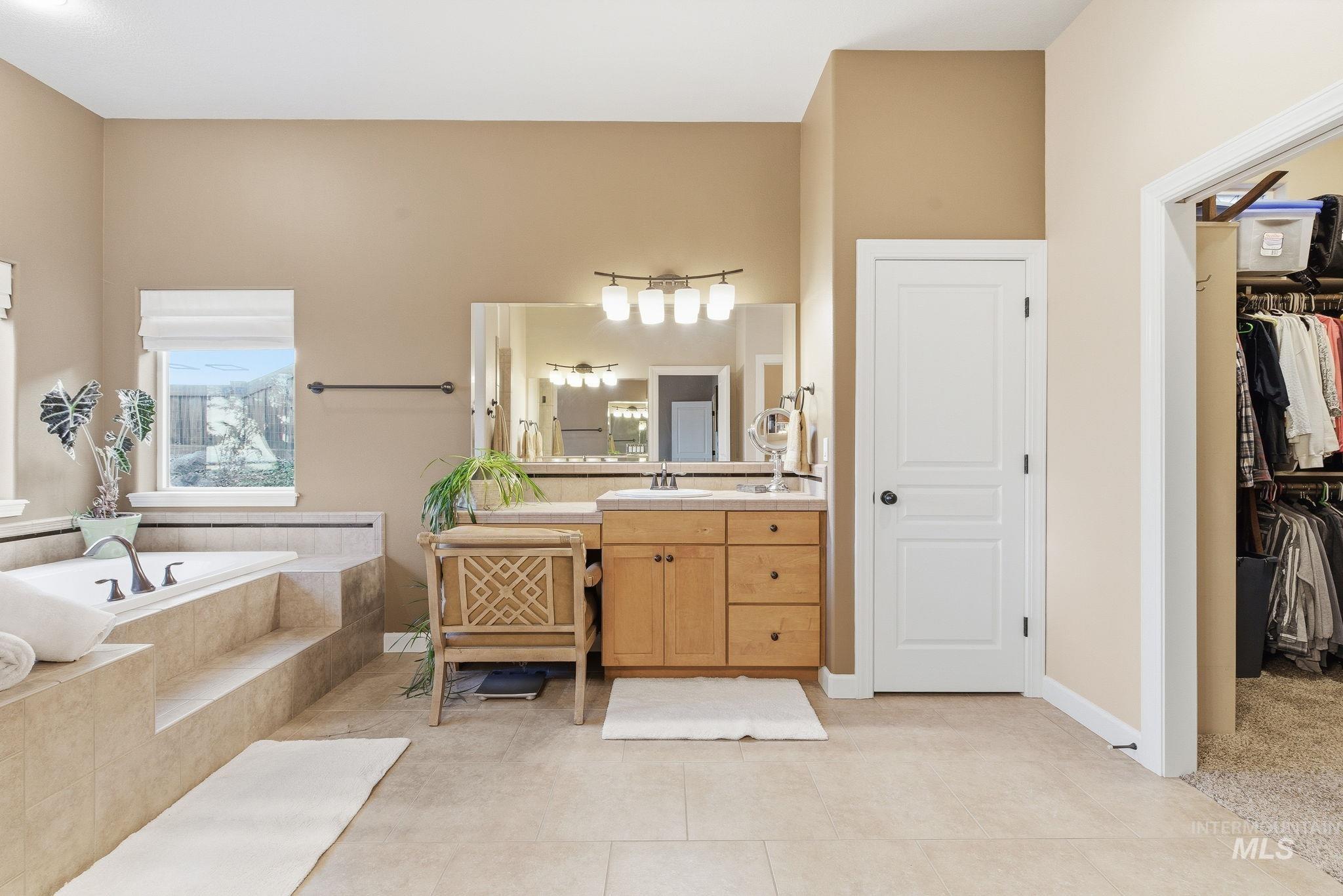 Bathroom featuring vanity, a spacious closet, a garden tub, and light tile patterned flooring