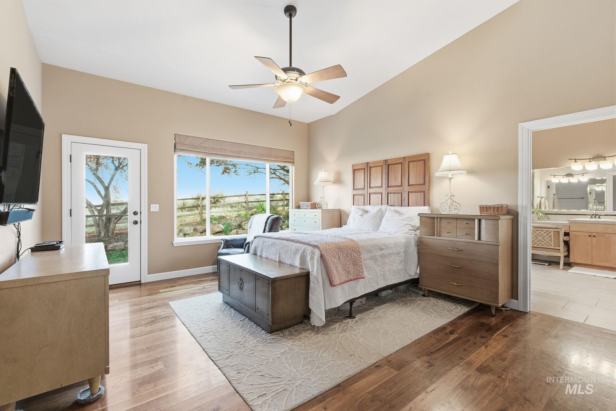 Bedroom with access to exterior, light wood finished floors, ceiling fan, high vaulted ceiling, and ensuite bath