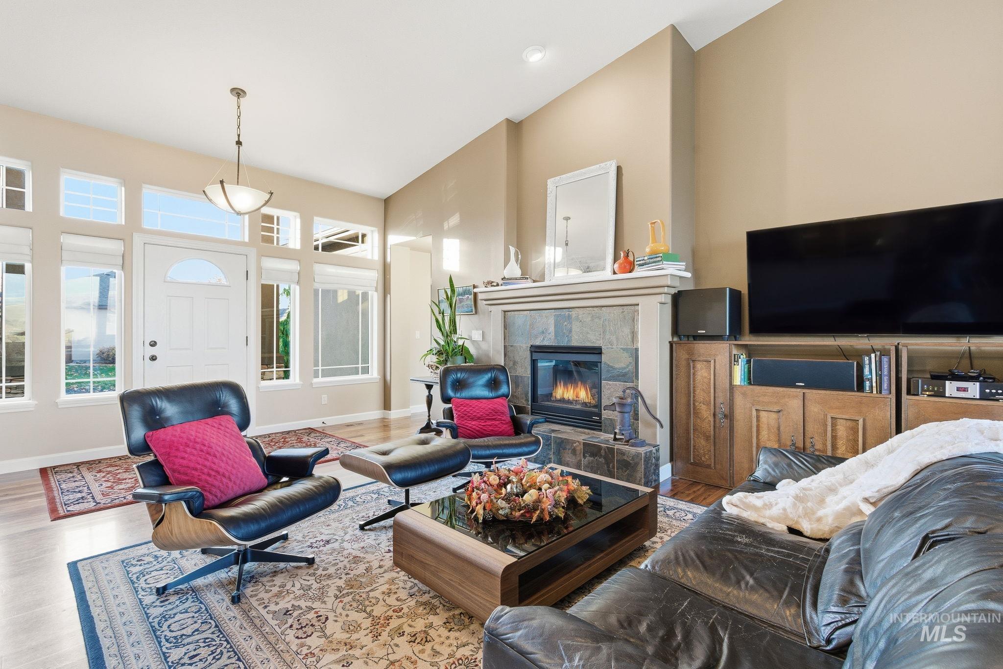 Living room with wood finished floors, a tiled fireplace, and a towering ceiling