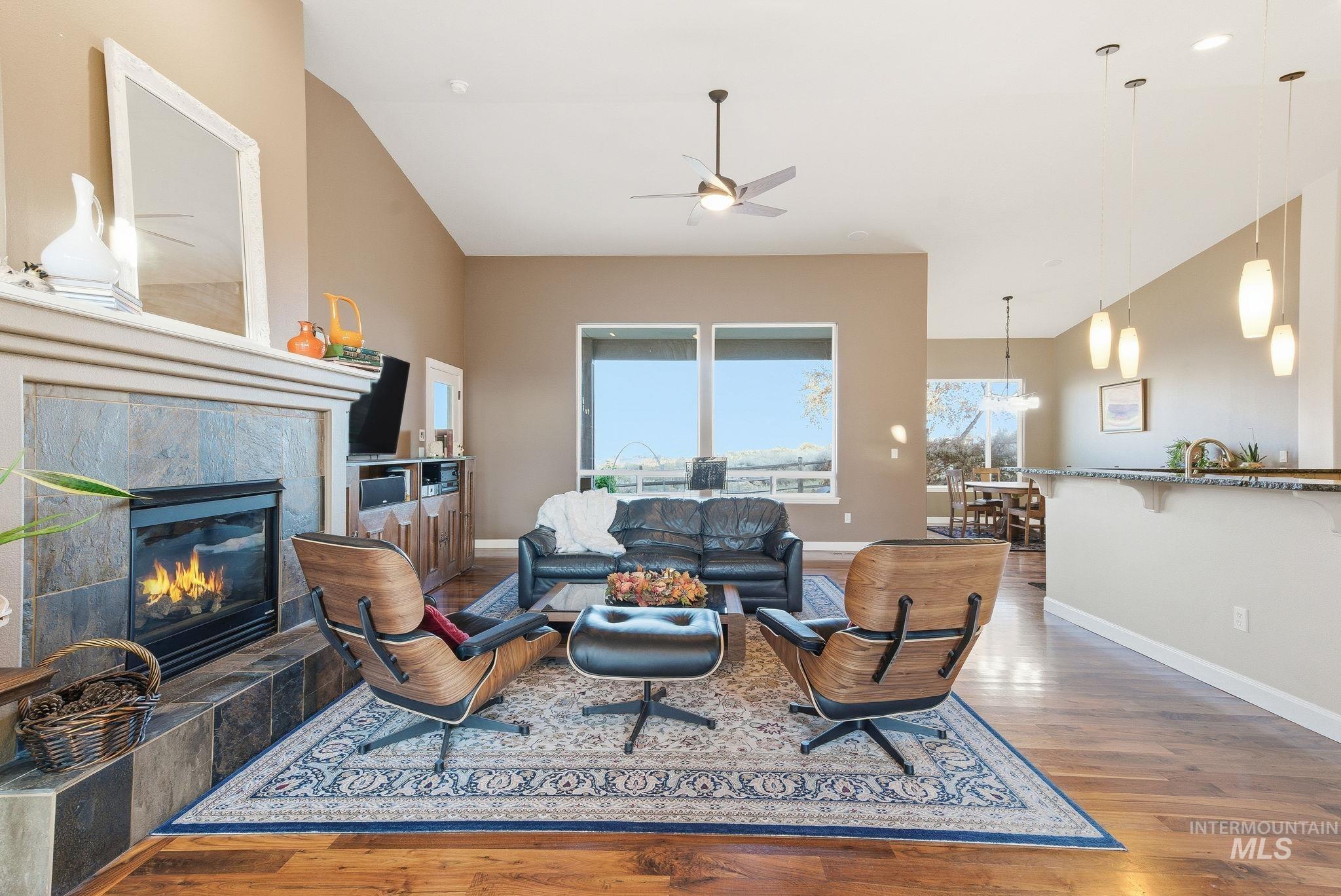 Living area with wood finished floors, high vaulted ceiling, a tile fireplace, and a ceiling fan