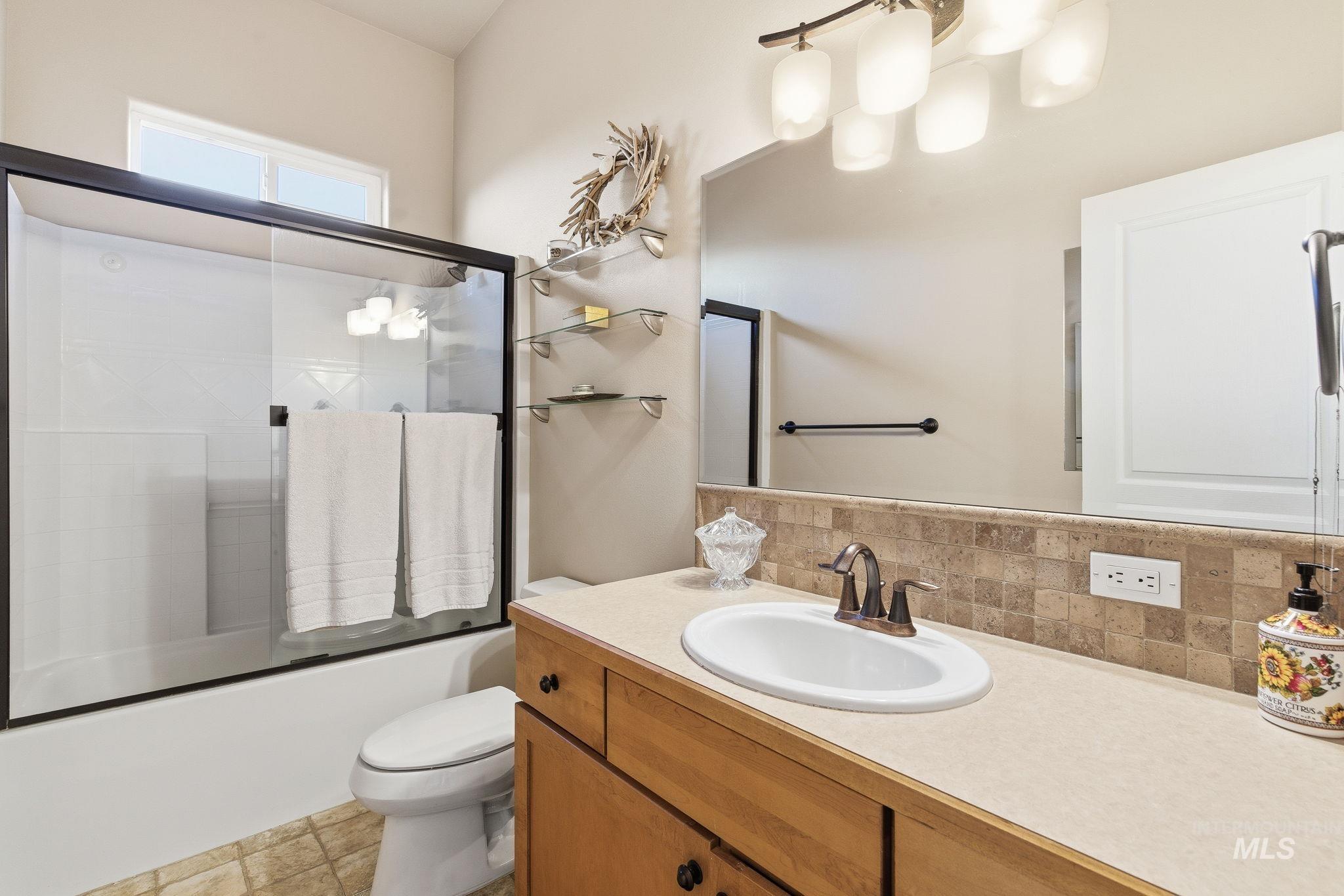 Full bathroom with combined bath / shower with glass door, vanity, backsplash, and light tile patterned floors