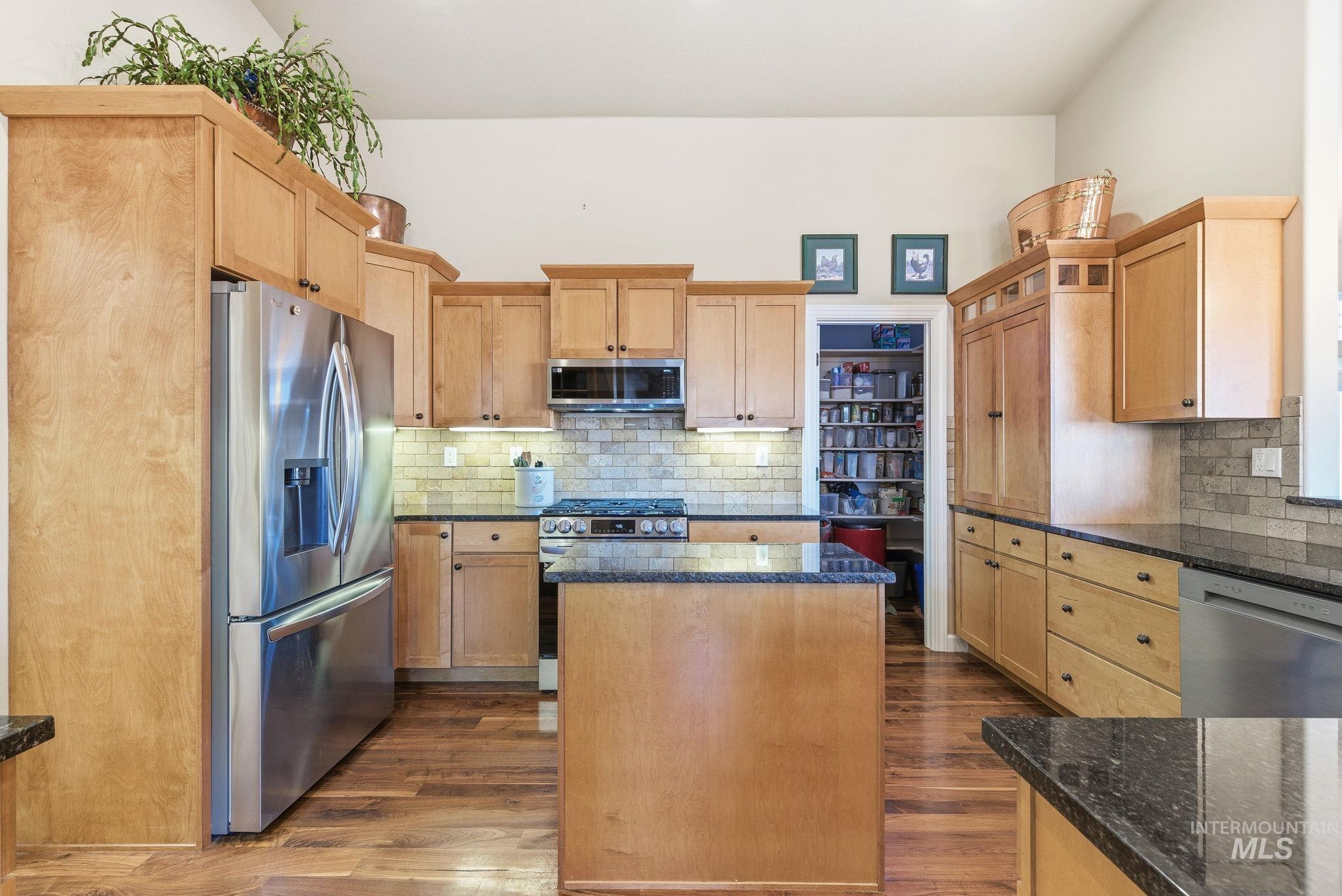 Kitchen featuring stainless steel appliances, dark wood-style flooring, a center island, and dark stone counters
