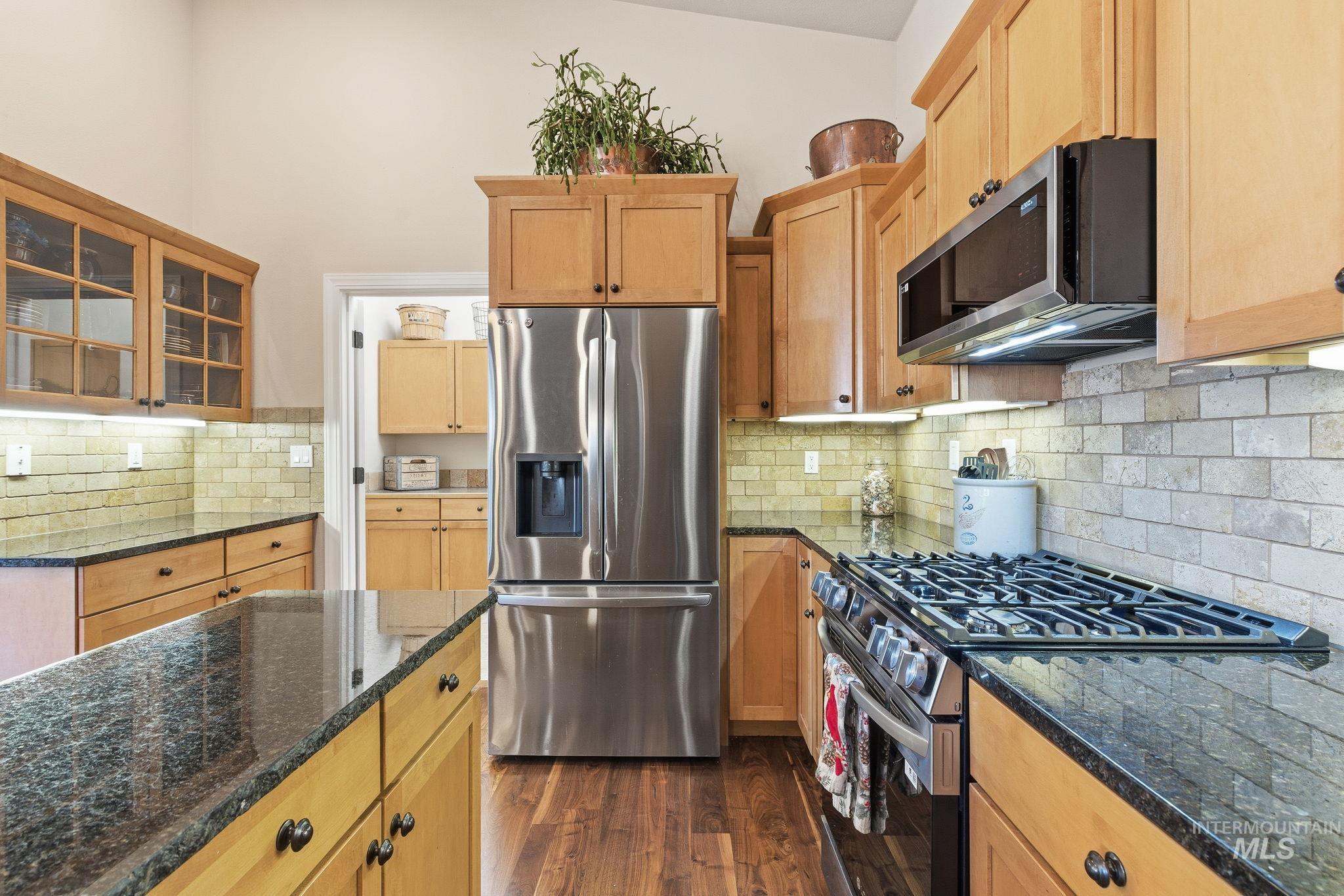 Kitchen with appliances with stainless steel finishes, tasteful backsplash, dark stone countertops, and glass insert cabinets