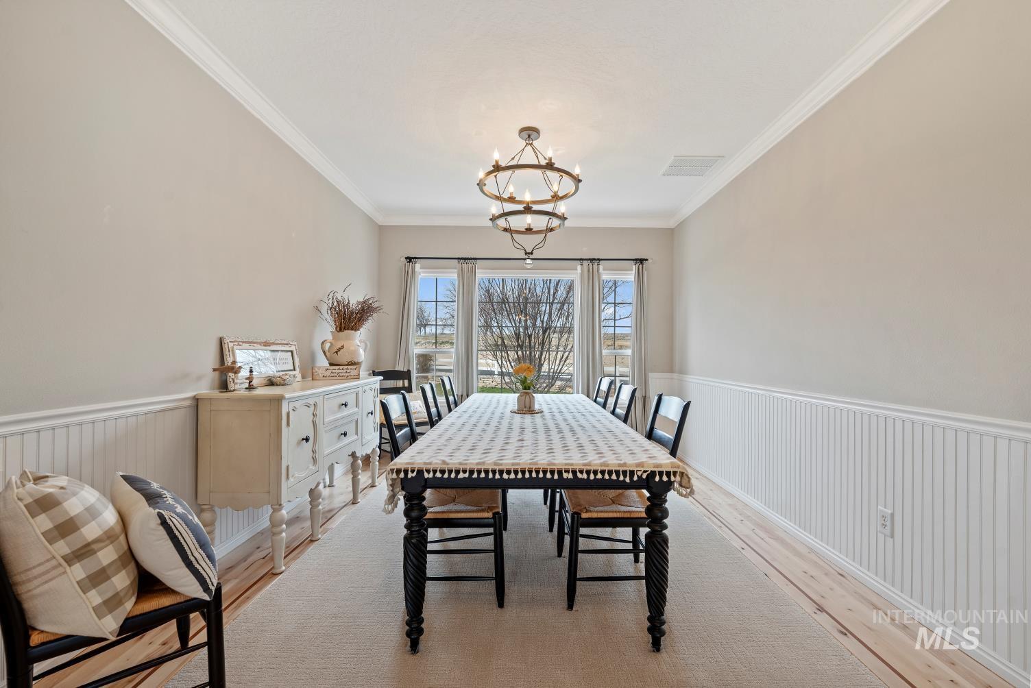Dining room featuring wainscoting, hardwood / wood-style floors, hanging lights, and crown molding