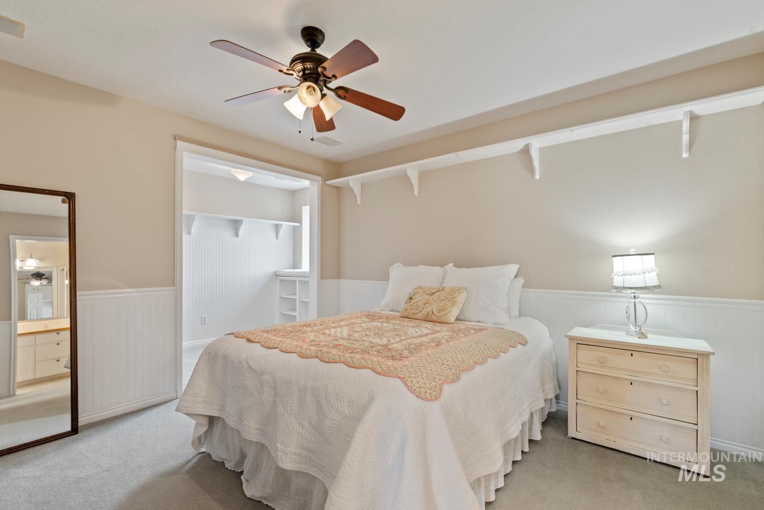 Bedroom with a wainscoted wall, ceiling fan, light colored carpet, and ensuite bathroom