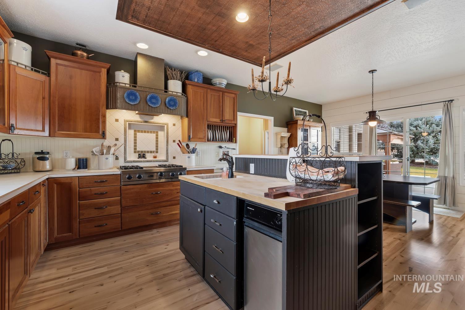 Kitchen featuring a center island with sink, decorative light fixtures, open shelves, wood counters, and light wood-style floors