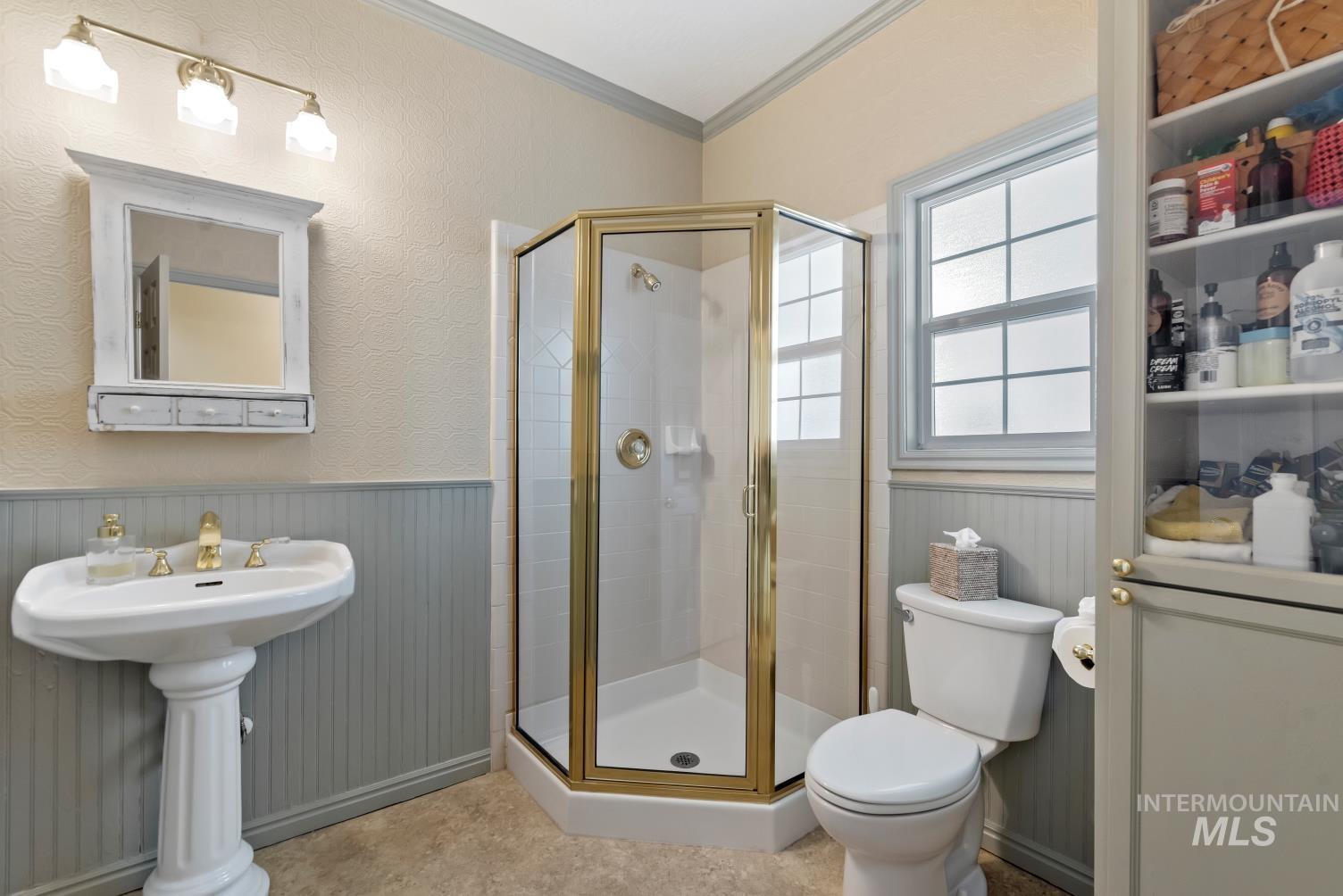 Bathroom with ornamental molding, wainscoting, and a shower stall