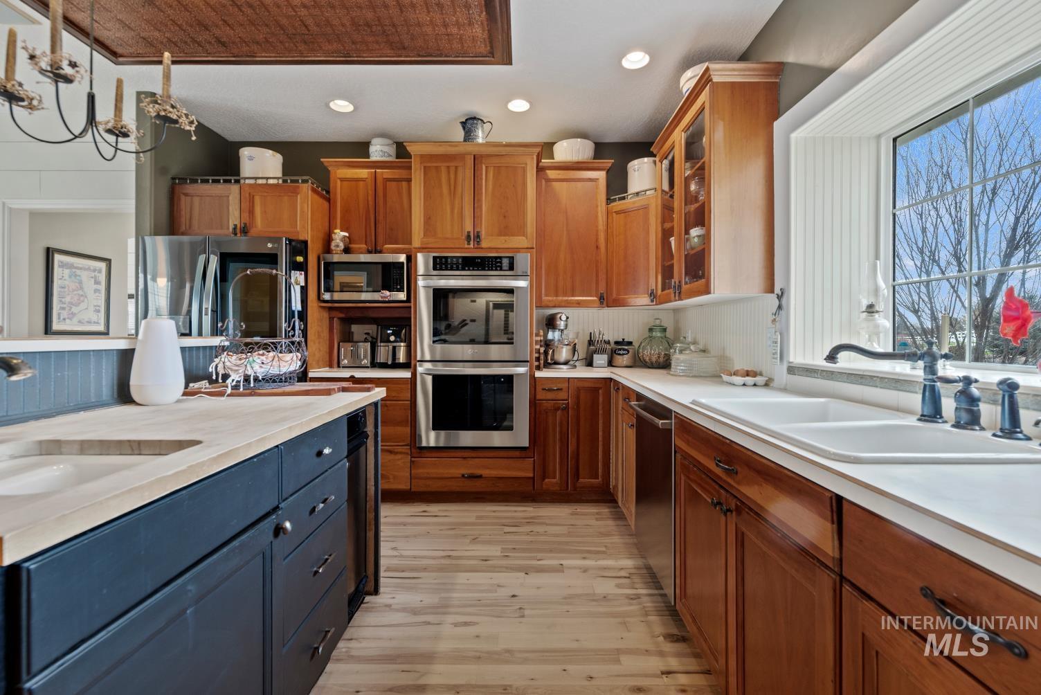 Kitchen with glass fronted cabinets, stainless steel appliances, tasteful backsplash, light wood-style floors, and suspended lighting