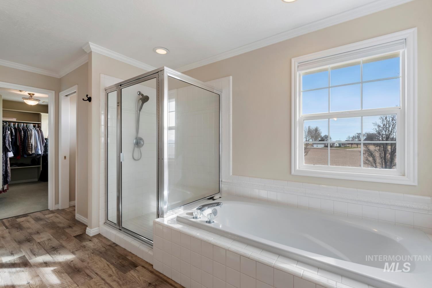Full bathroom with a walk in closet, a garden tub, a shower stall, ornamental molding, and wood finished floors