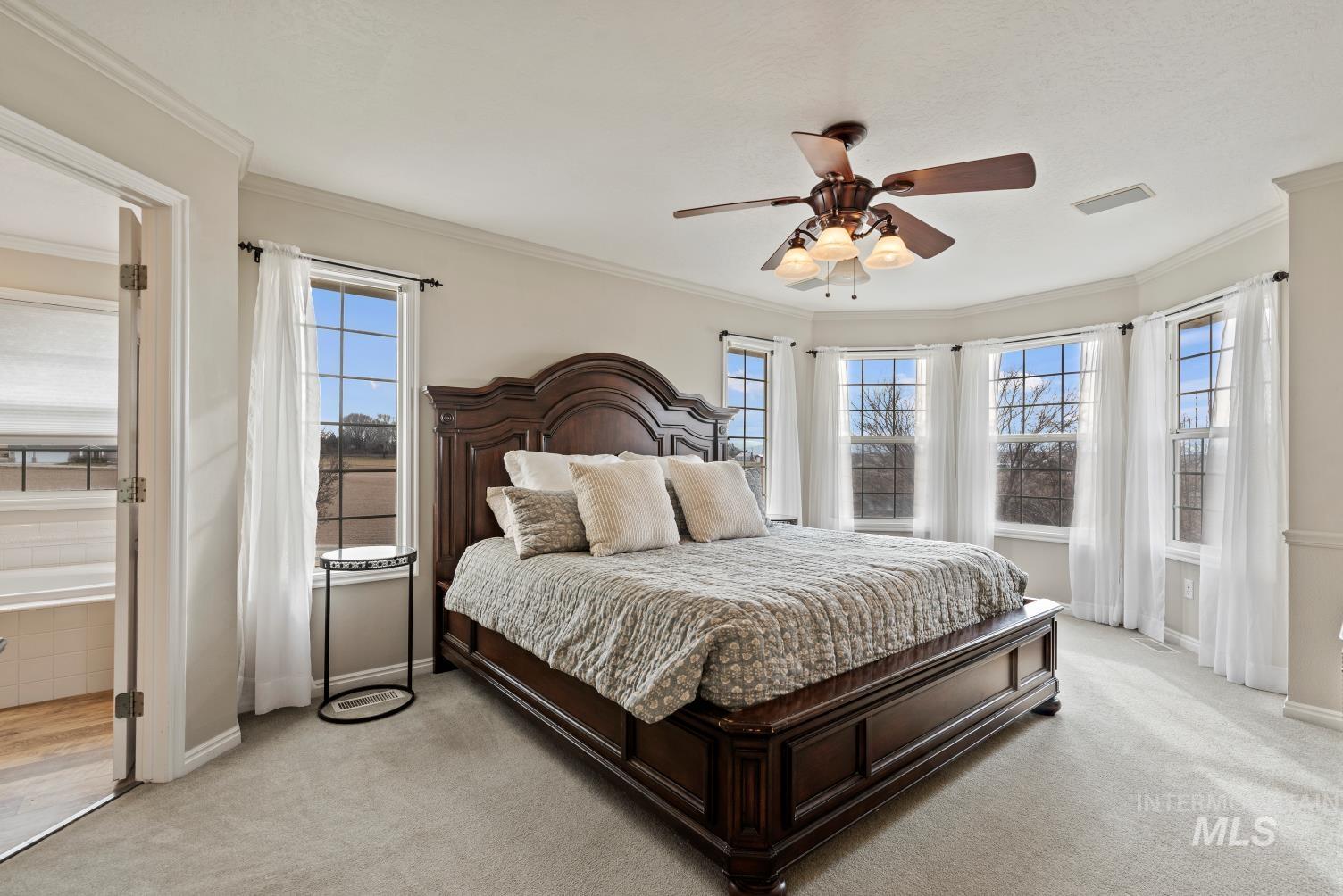 Bedroom with ceiling fan, ornamental molding, and light carpet