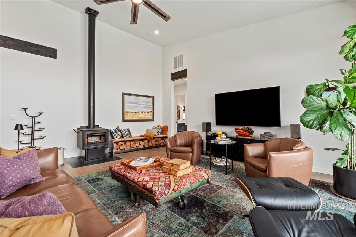 Living area featuring a wood stove, ceiling fan, wood finished floors, a towering ceiling, and recessed lighting