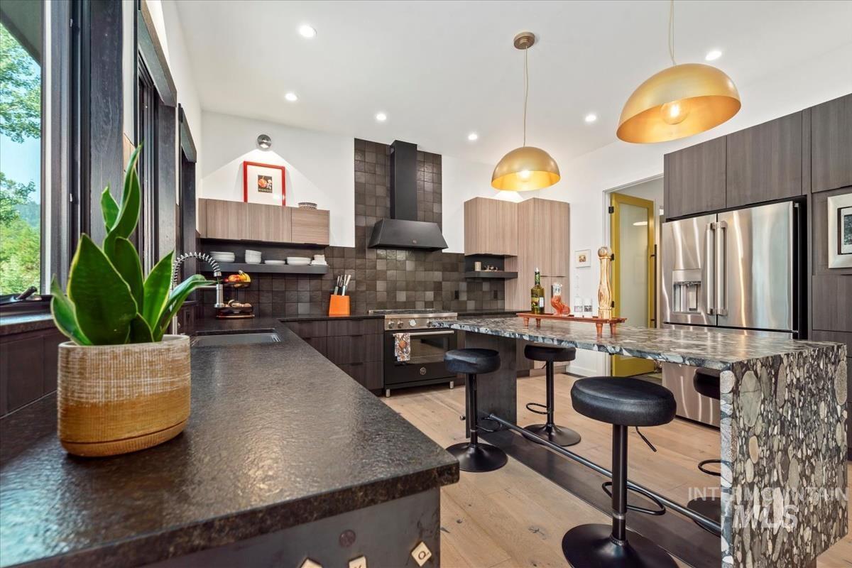 Kitchen with a breakfast bar area, modern cabinets, light wood-style flooring, premium appliances, and wall chimney exhaust hood