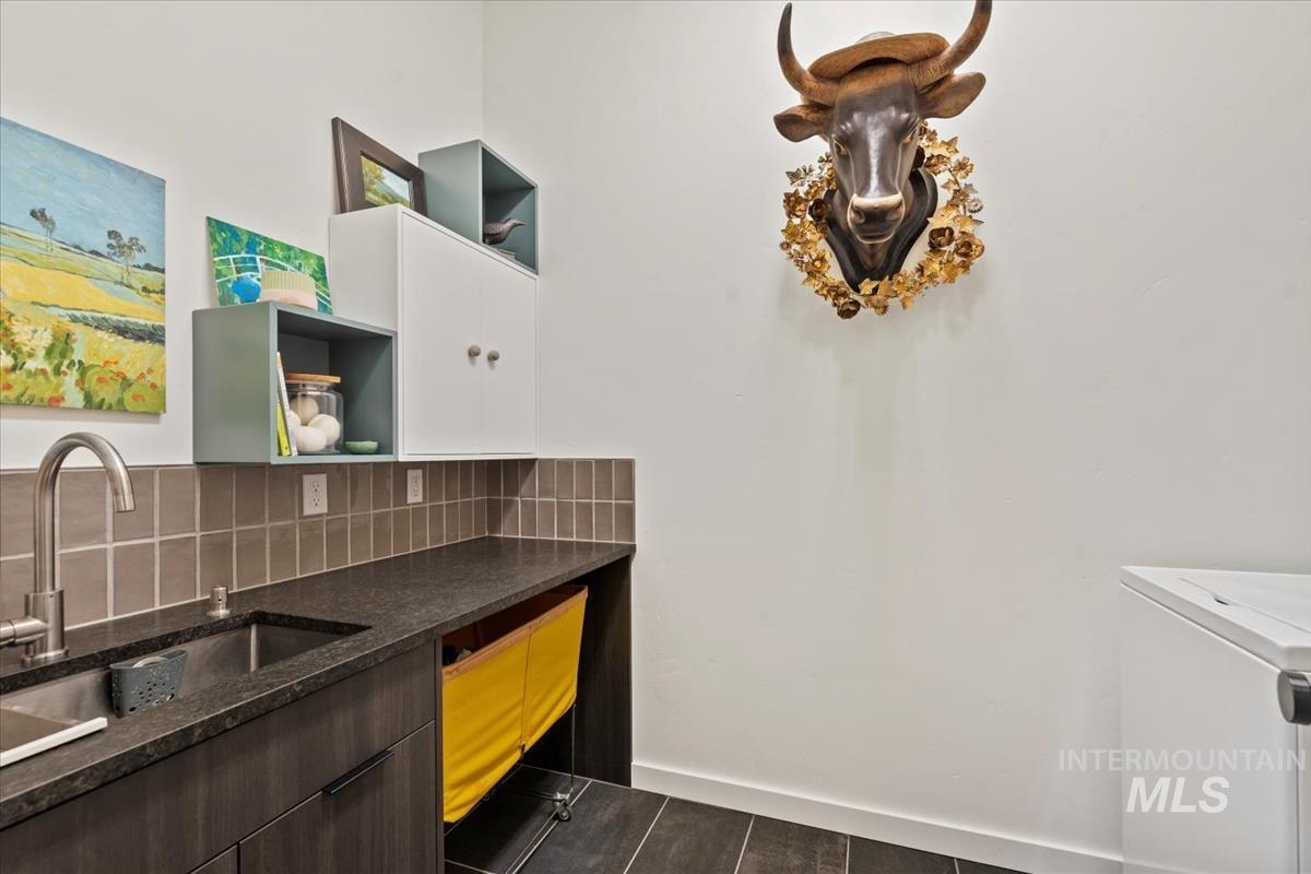 Decorative backsplash, dark brown cabinets, washer / clothes dryer, and dark stone countertops