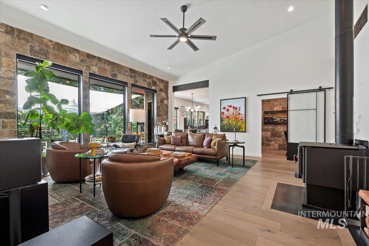 Living room featuring wood-type flooring, ceiling fan, a wood stove, lofted ceiling, and recessed lighting