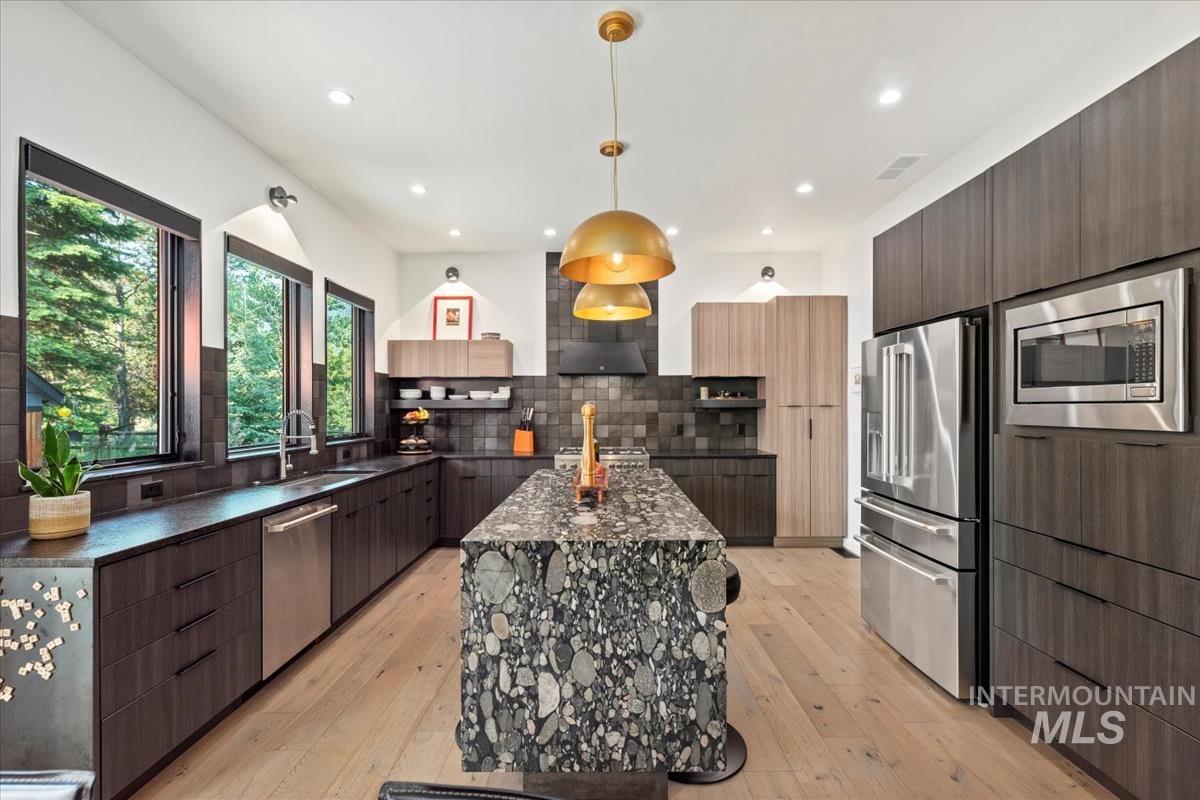 Kitchen with modern cabinets, light wood-style floors, stainless steel appliances, a center island, and decorative light fixtures