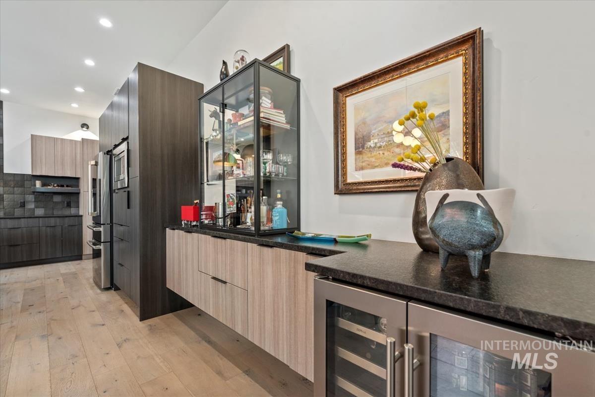 Indoor dry bar with beverage cooler, light wood-style flooring, recessed lighting, and stainless steel fridge with ice dispenser