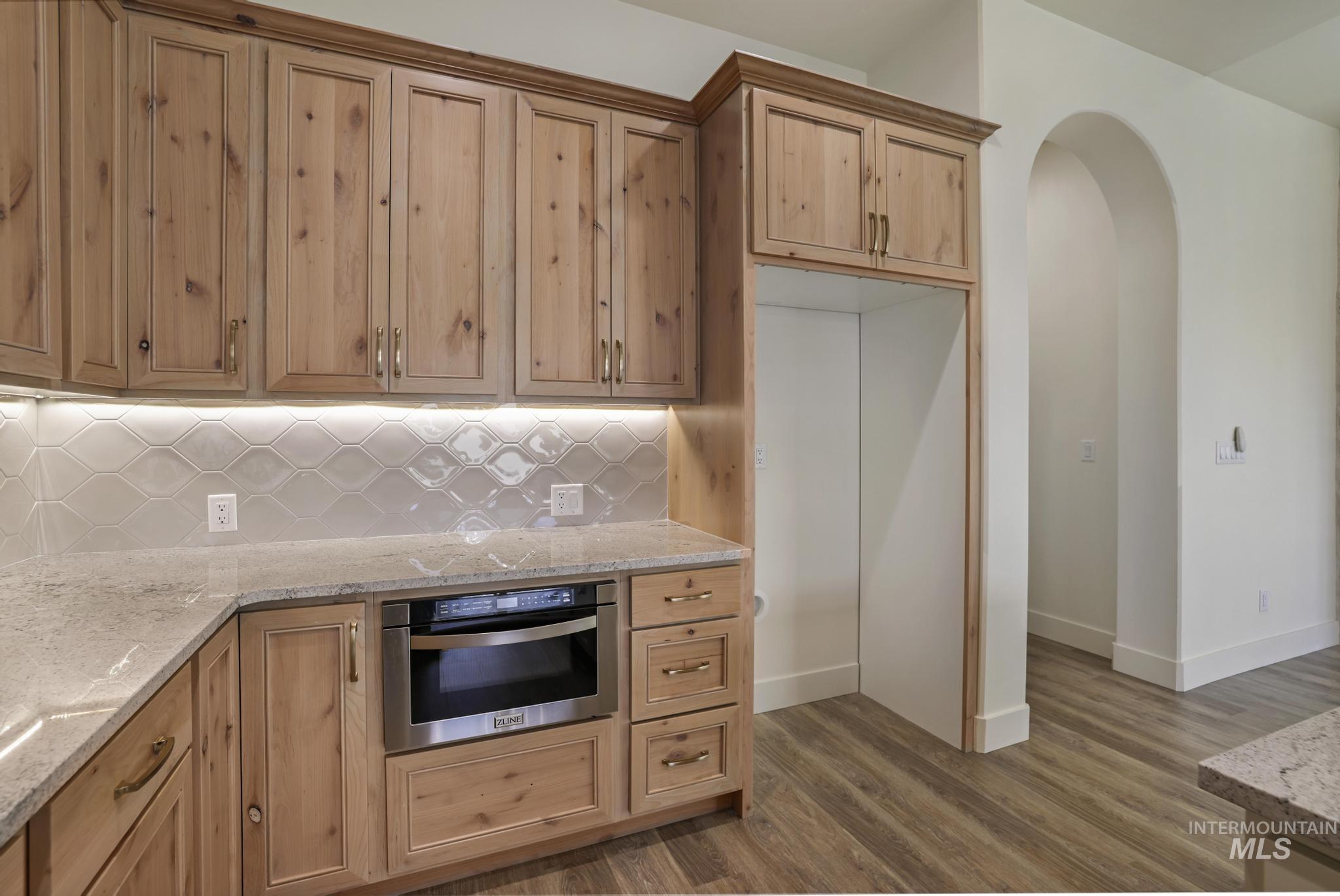 Kitchen featuring light stone counters, oven, dark wood-style floors, decorative backsplash, and arched walkways