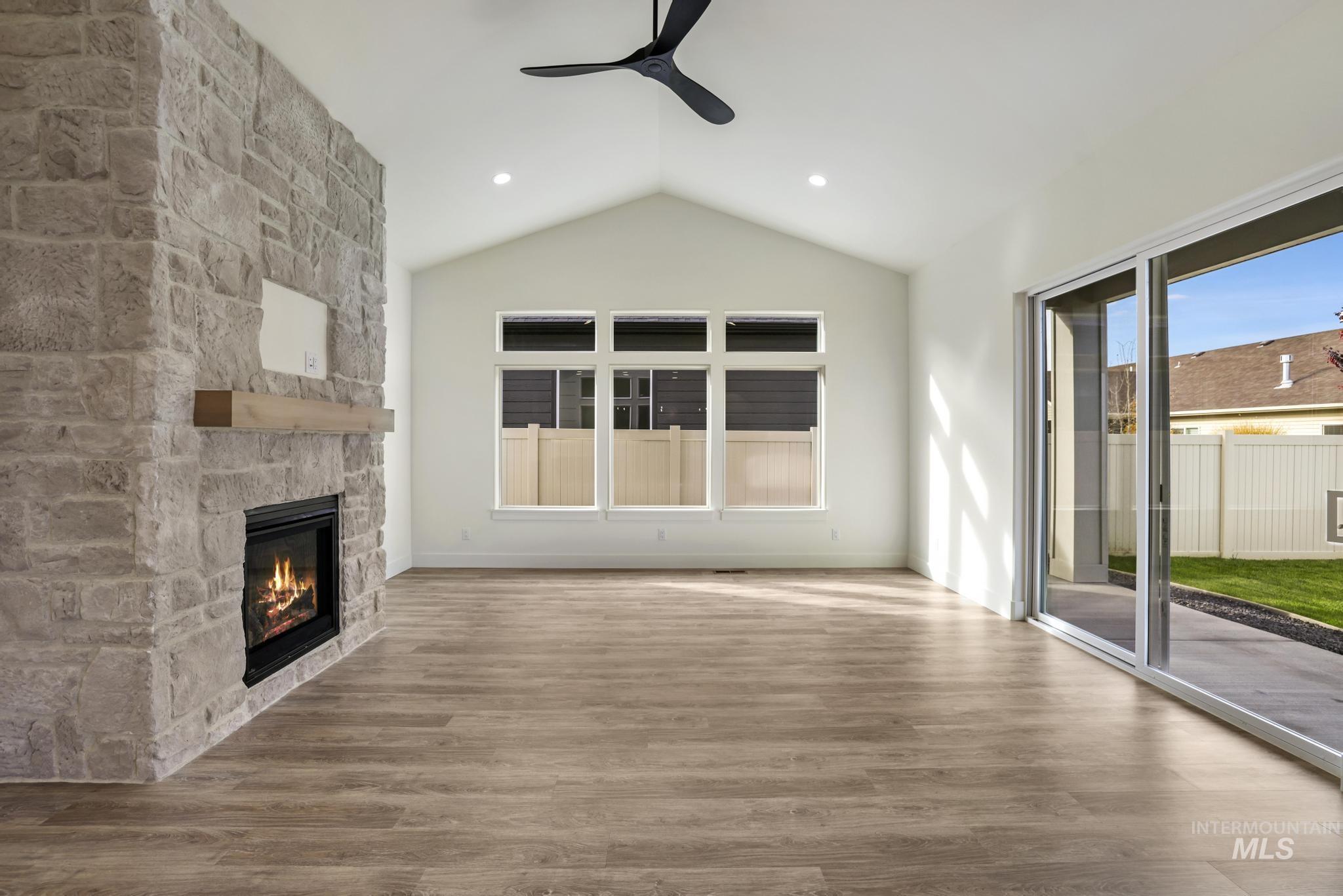 Unfurnished living room with vaulted ceiling, wood finished floors, ceiling fan, a stone fireplace, and recessed lighting
