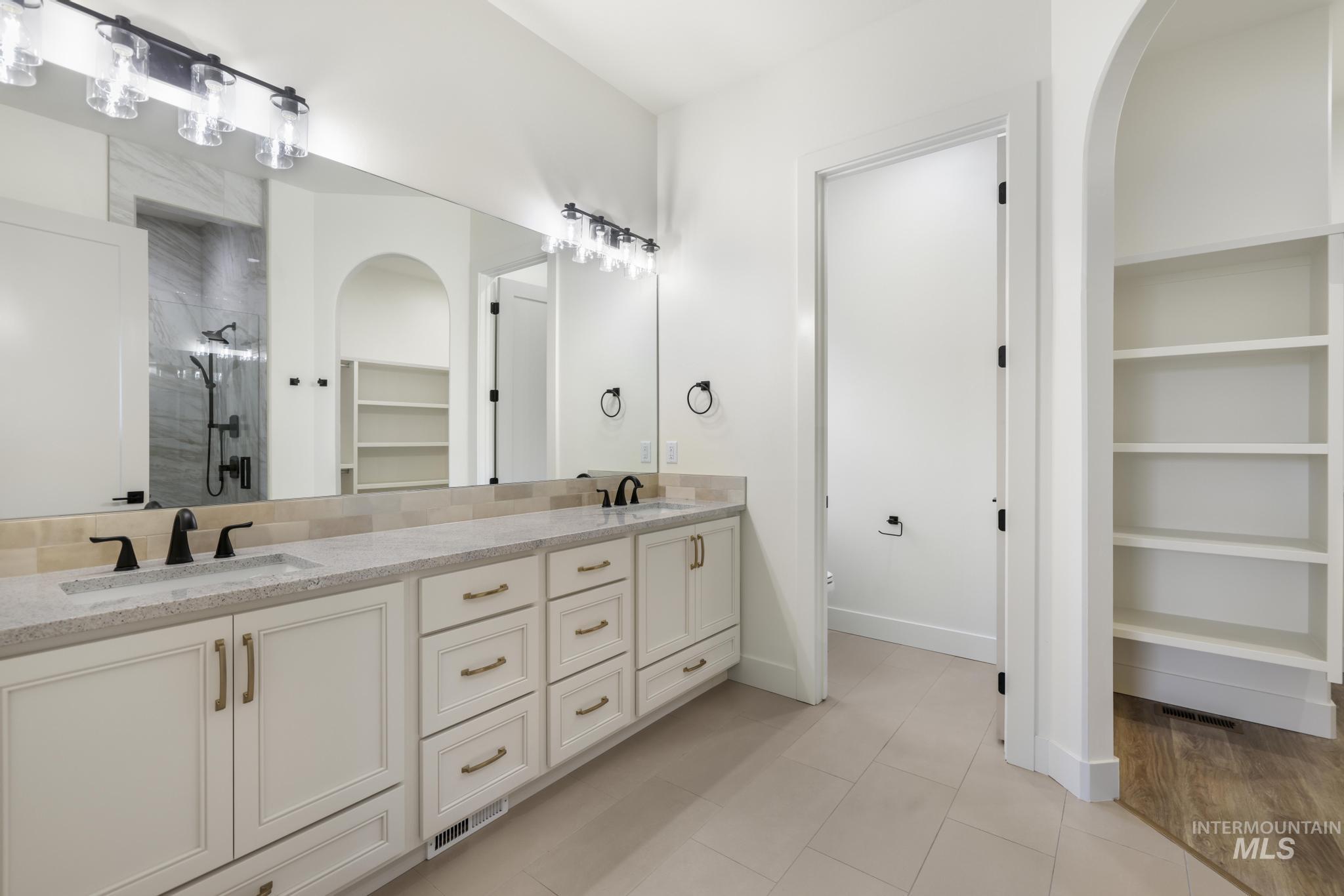 Bathroom featuring a walk in closet, double vanity, a stall shower, built in shelves, and light tile patterned floors