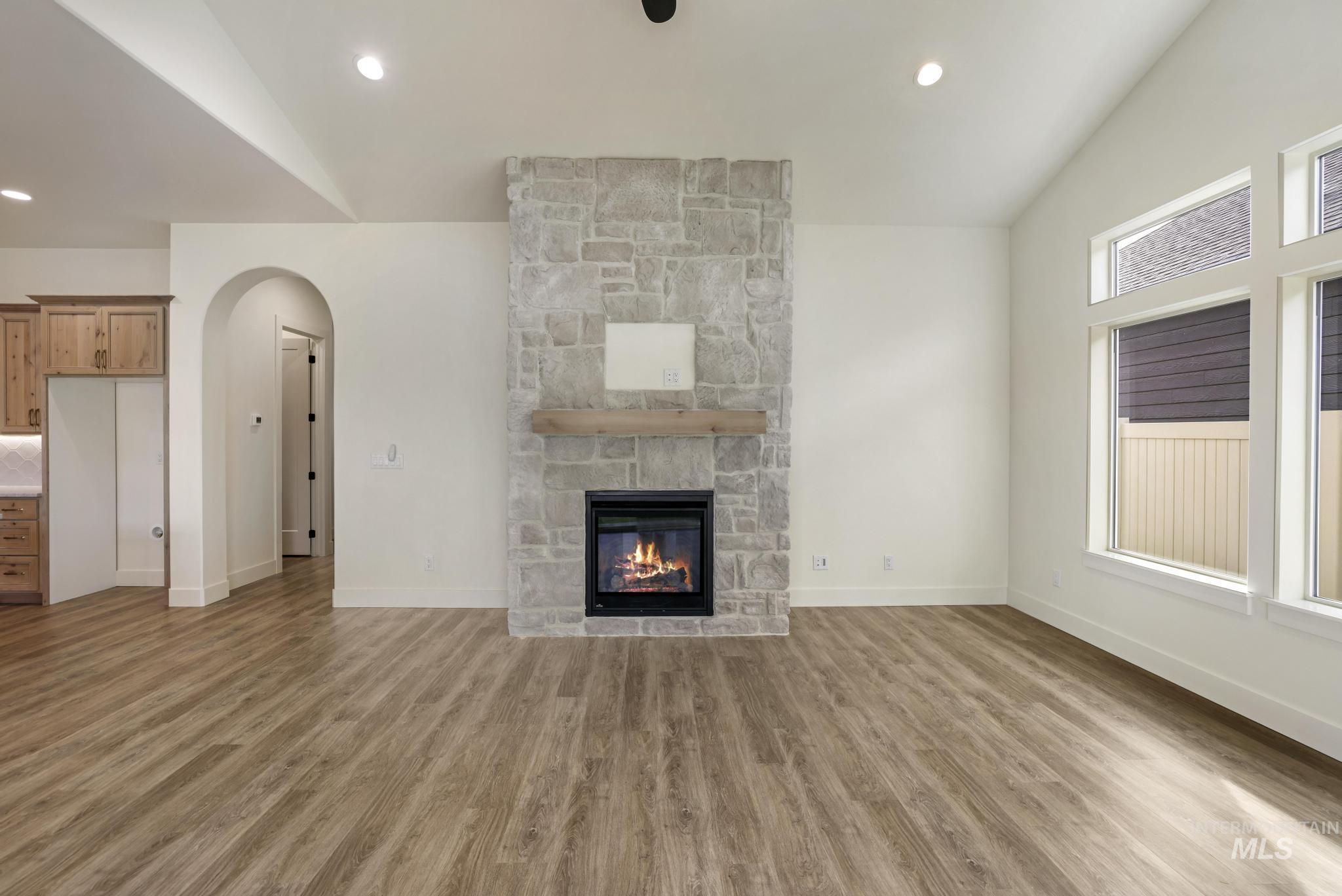 Unfurnished living room with recessed lighting, arched walkways, light wood-type flooring, a stone fireplace, and high vaulted ceiling